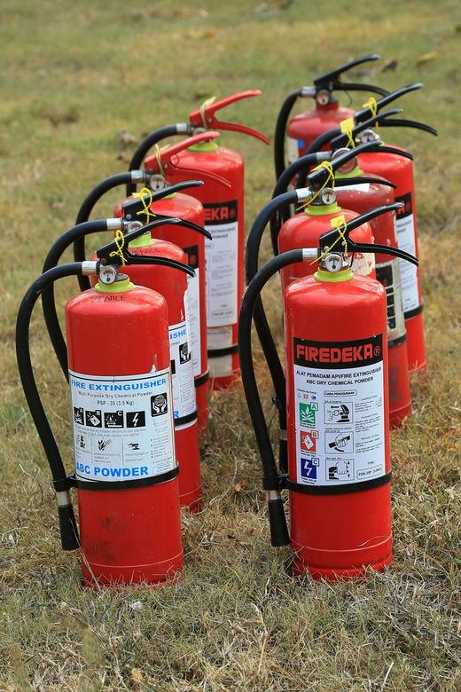 Several bright red fire extinguishers standing in rows on grass.