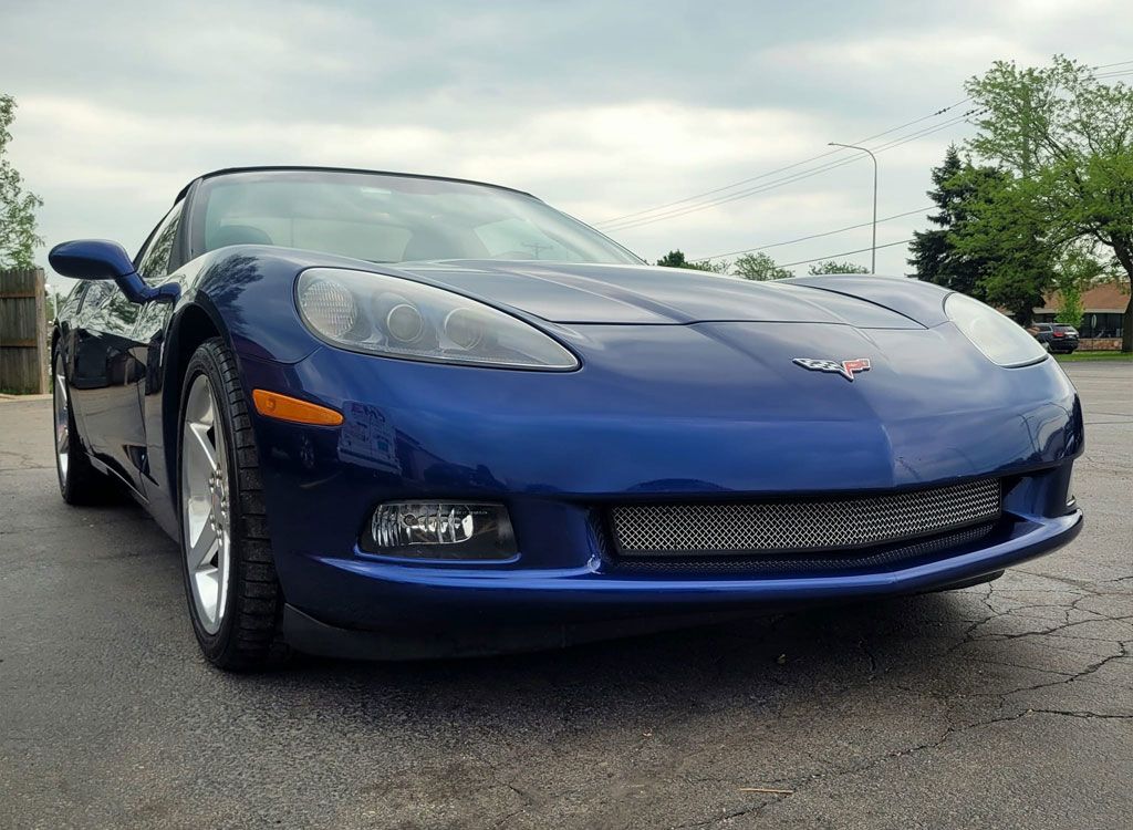 Blue Corvette sports car parked on wet asphalt under an overcast sky.