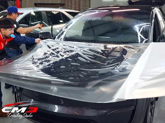 Clear bra installation on black car hood with protective film and detailing soap application.