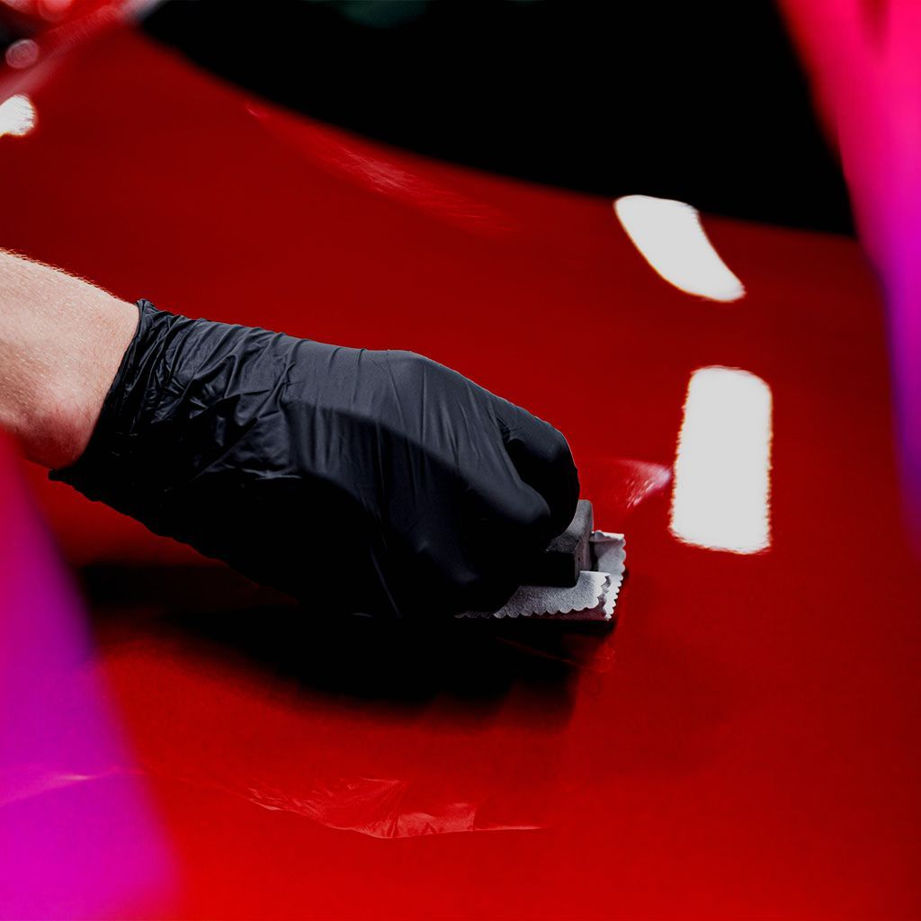 A person wearing black gloves is polishing a red car.