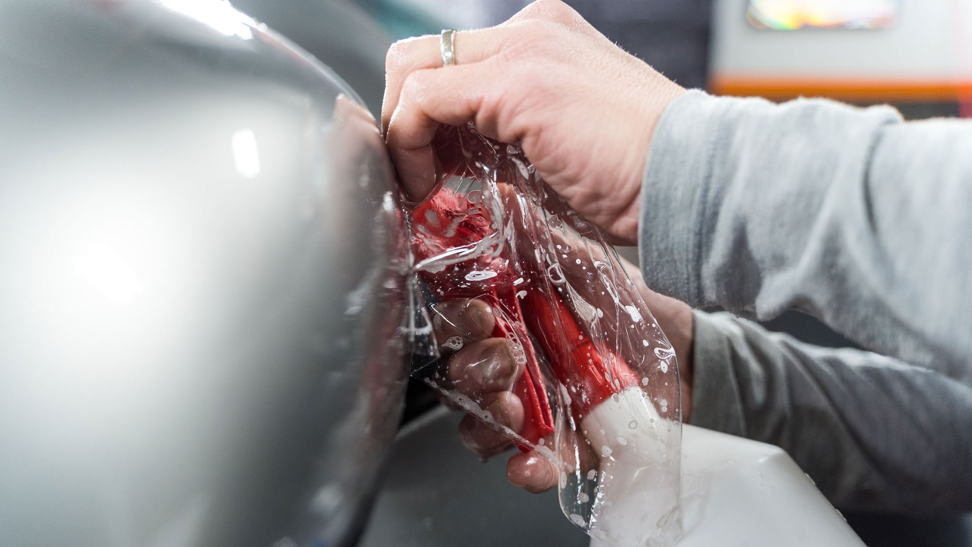 A person's hands are wrapping red and white item in clear plastic, near a curved, gray surface.