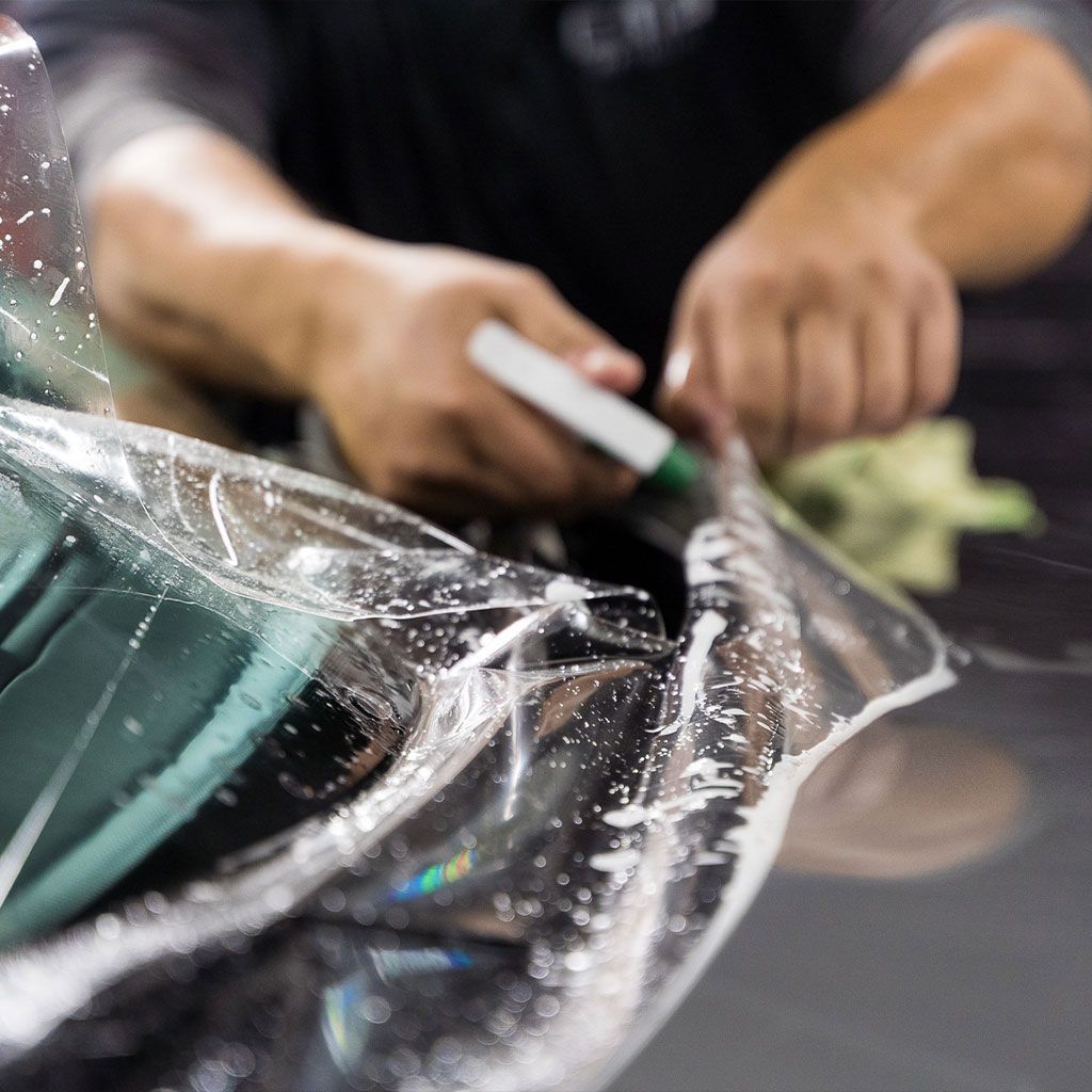 Person applying clear protective film to a car's surface with a marker, close-up view.