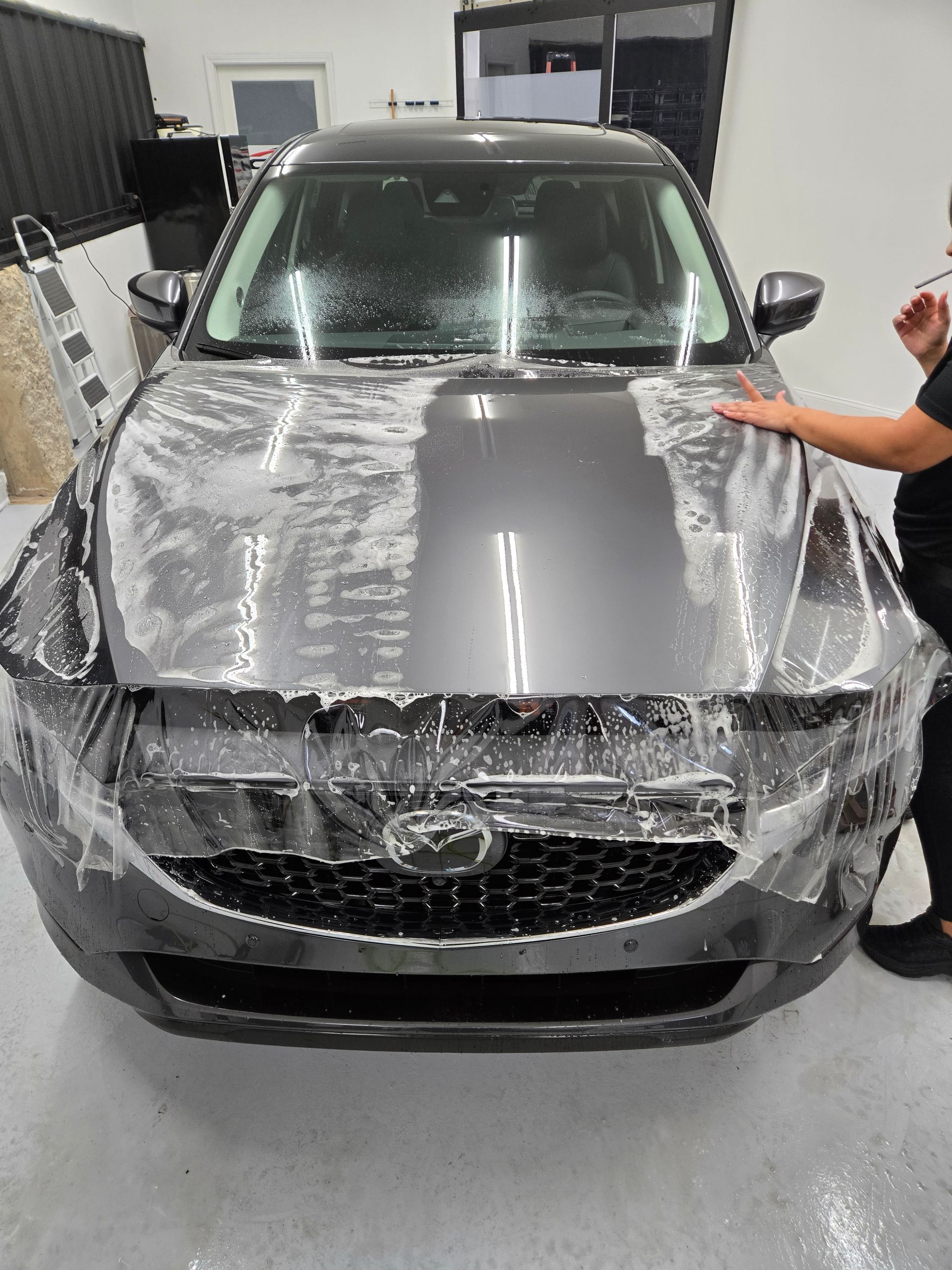 Technician smoothing clear bra paint protection film over a car's hood during installation