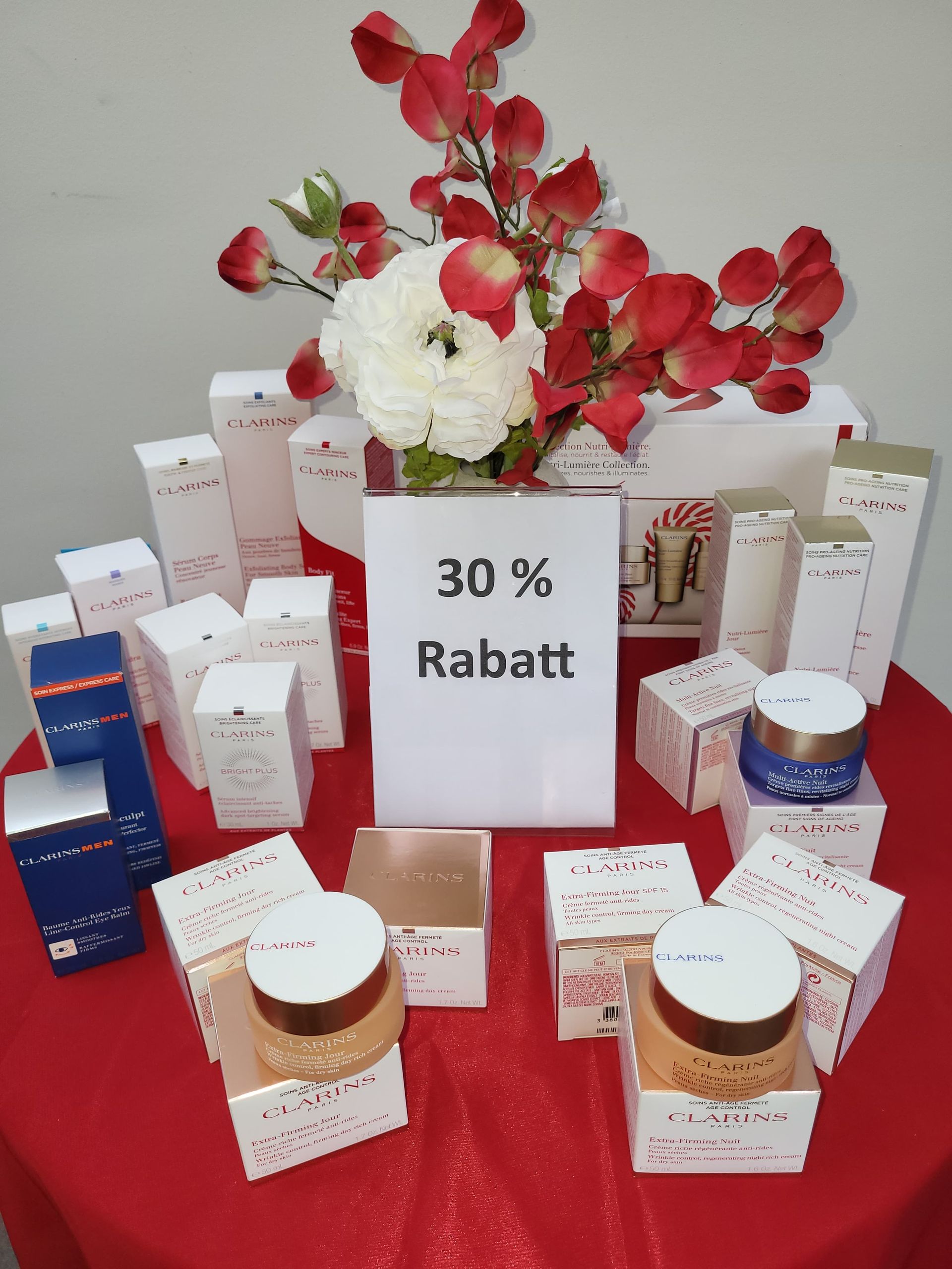 Schönheitsprodukte auf roter Tischdecke mit weissem Schild mit der Aufschrift «30 % Rabatt» und rot-weissen Blumen.