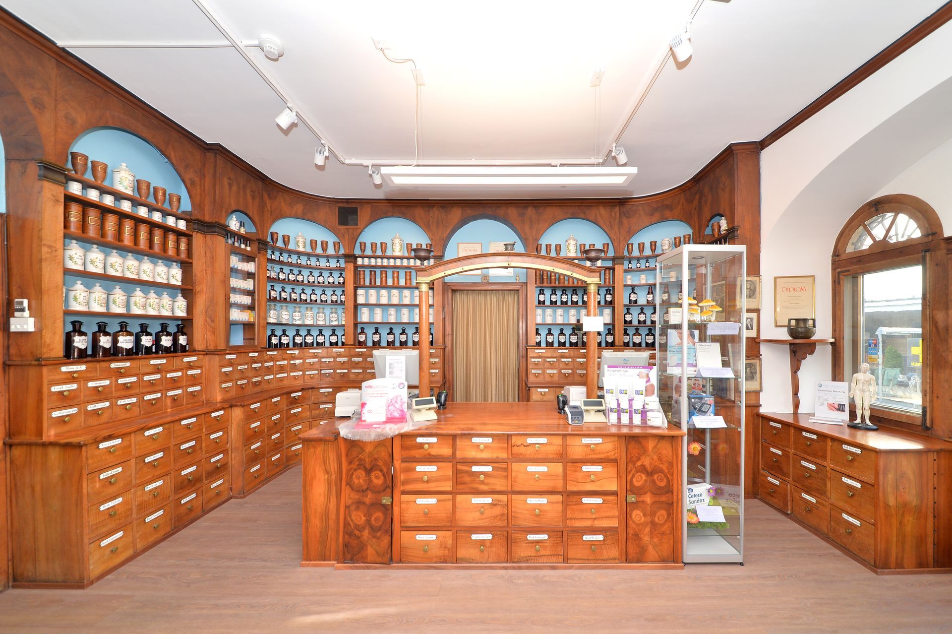 Holzgetäfelte Apothekerhandlung mit Regalen voller Gläser und Flaschen, Verkaufstheke und Bogenfenstern