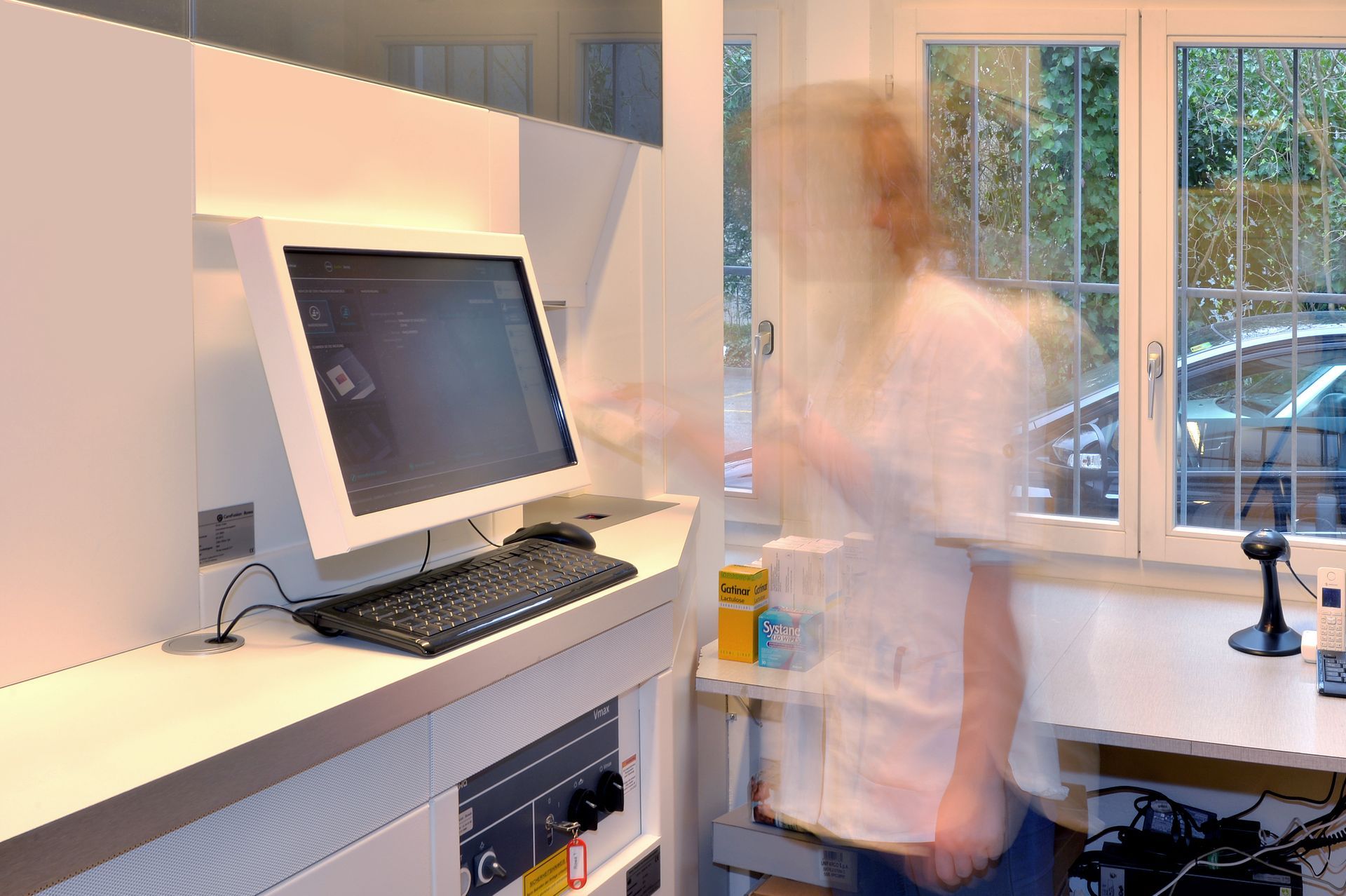 Verschwommene Person steht an einem Schreibtisch mit einem Desktop-Computer in einem hellen Büro oder Heimarbeitsplatz.