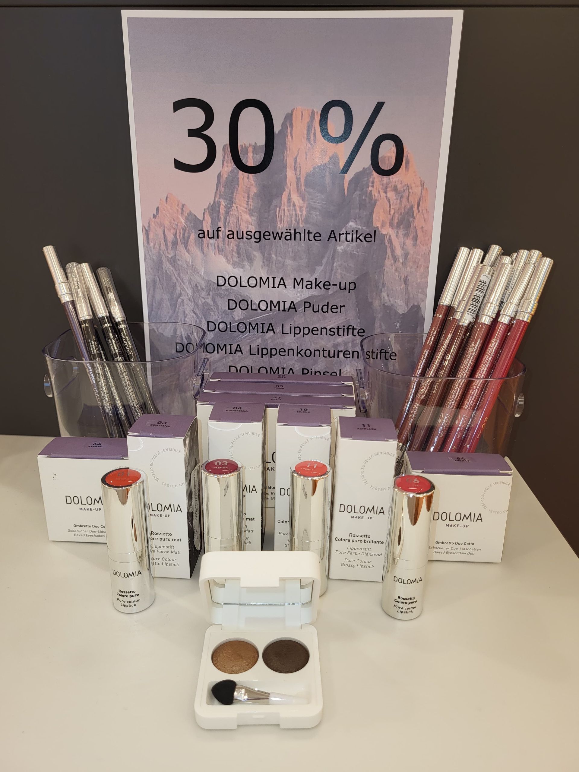 Kosmetikdisplay mit 30%-Rabatt-Schild, Hautpflegetuben, Paletten und Make-up-Pinseln auf einem Tisch