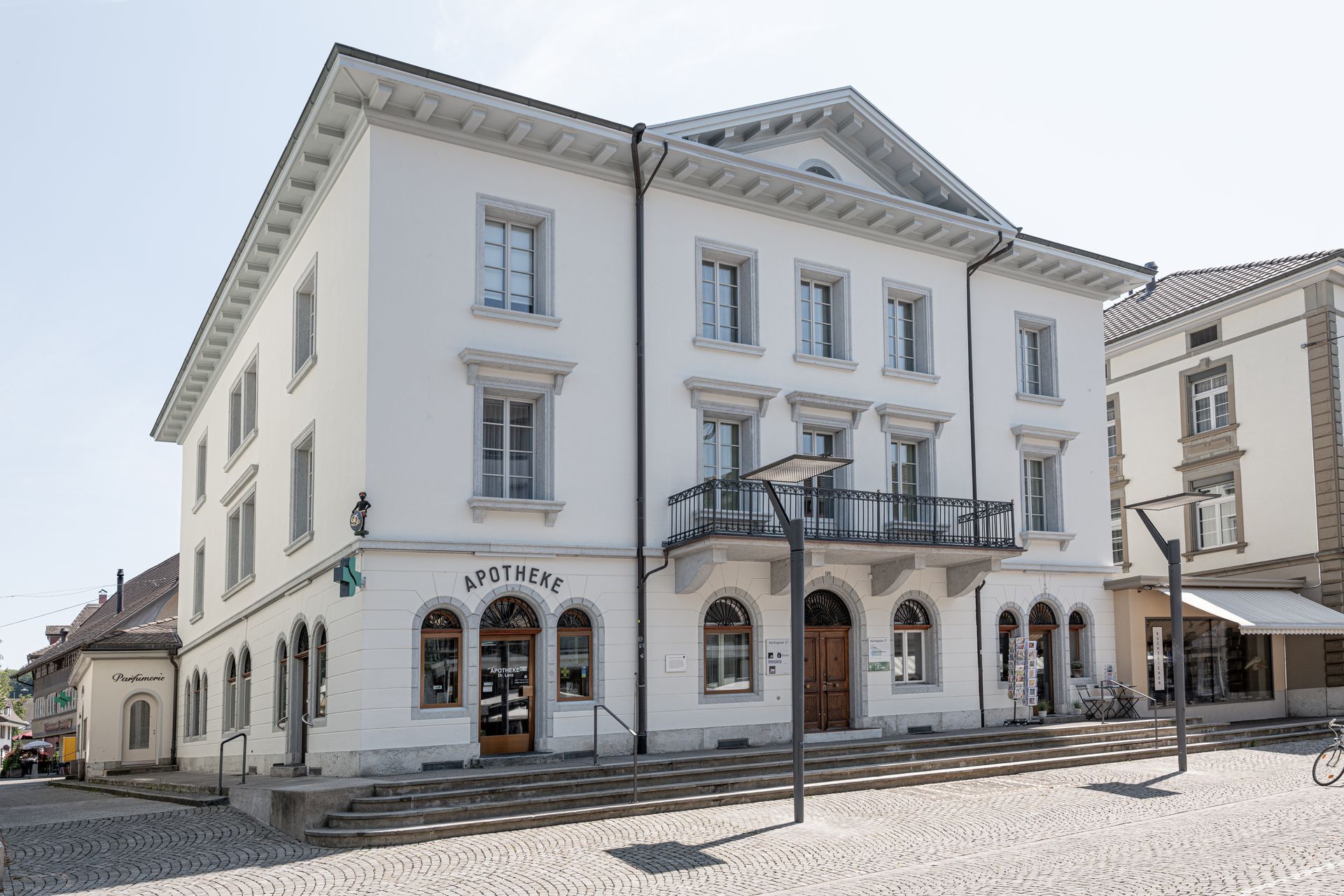Weisses historisches Gebäude mit Bogenfenstern und Balkonen an einer sonnigen Kopfsteinpflasterstrasse