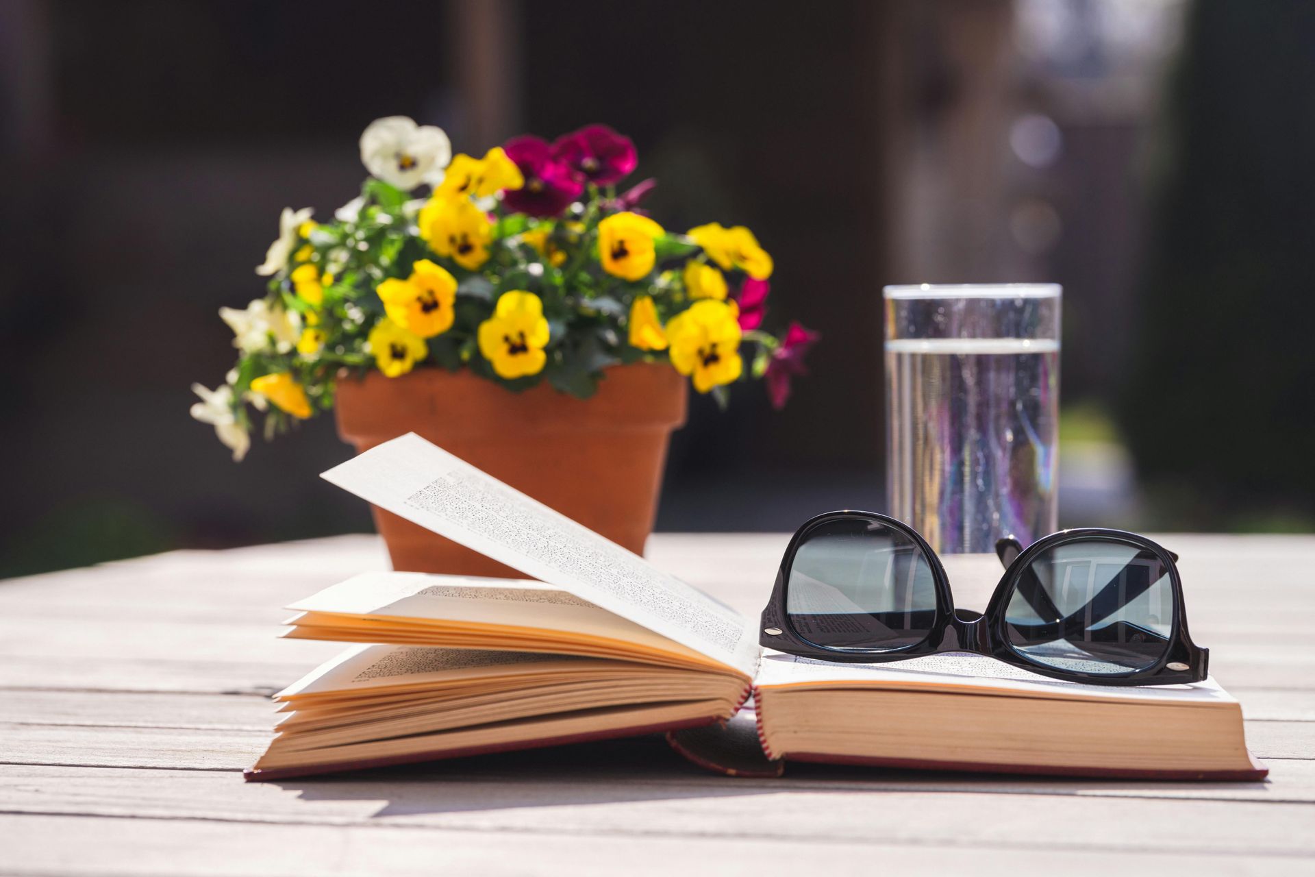 Ein offenes Buch, Gläser, Blumen und ein Glas Wasser auf einem Holztisch