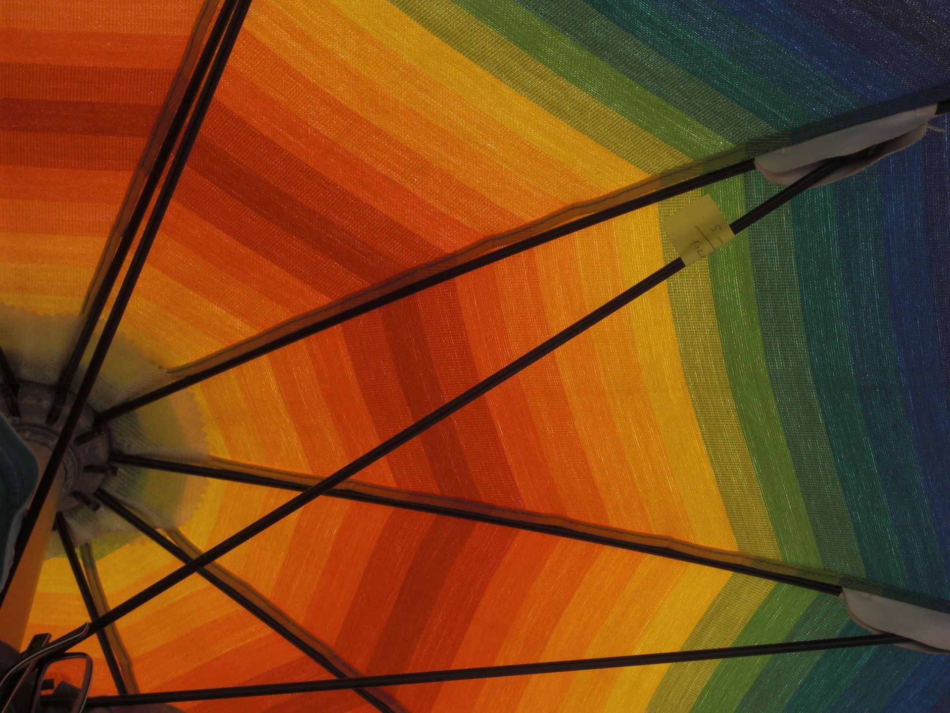 Regenbogenfarbenes Schirmdach, von unten betrachtet, mit schwarzen Speichen und metallischen Spitzen