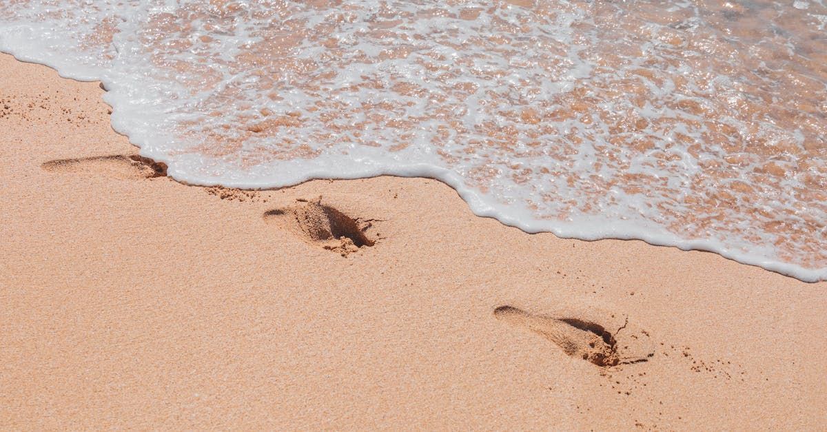 Fussabdrücke im nassen Sand nahe einer schäumenden Küste