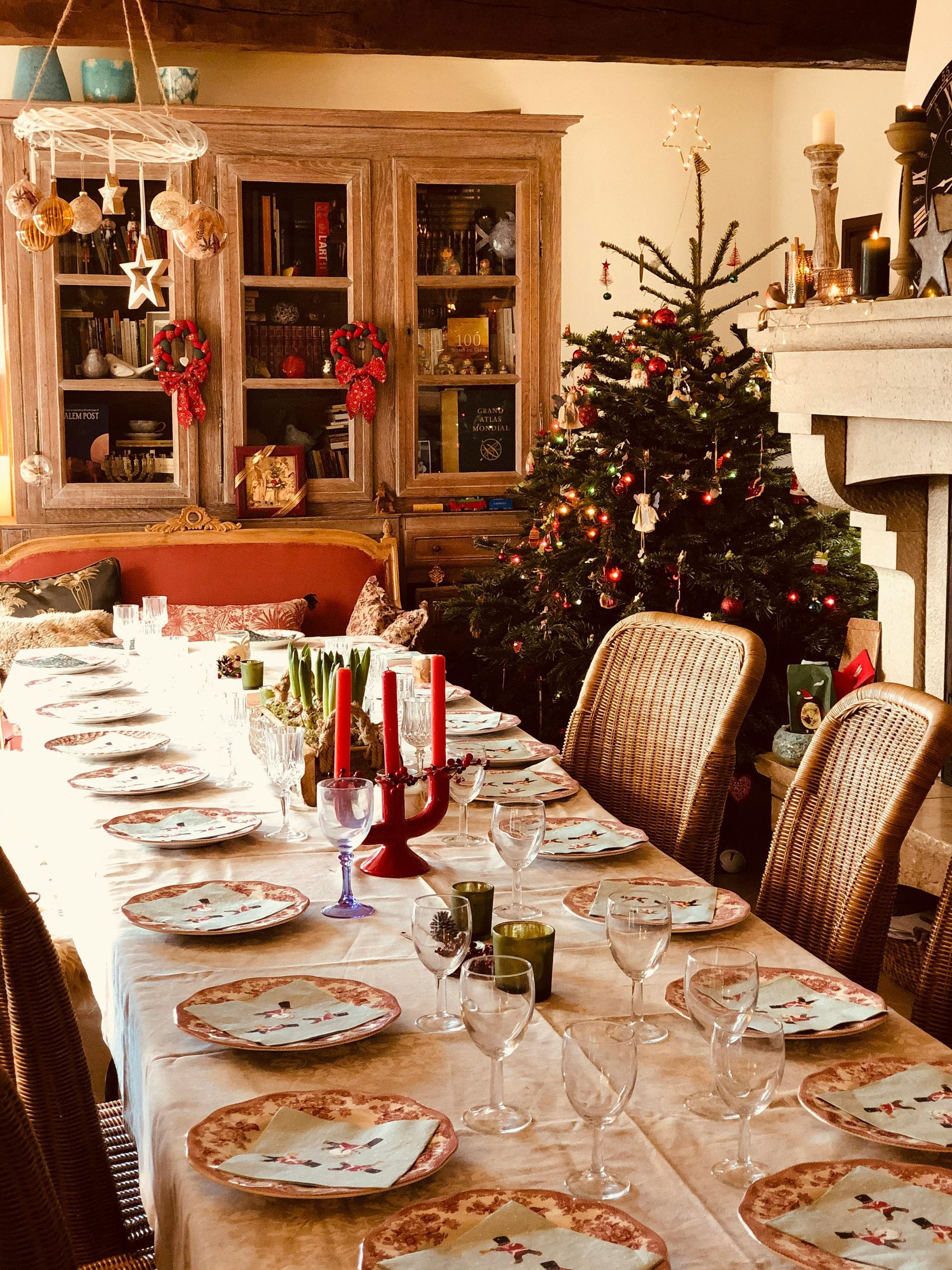 Ein festlich gedeckter Esstisch für das Weihnachtsessen steht neben einem geschmückten Baum und einem Schrank.