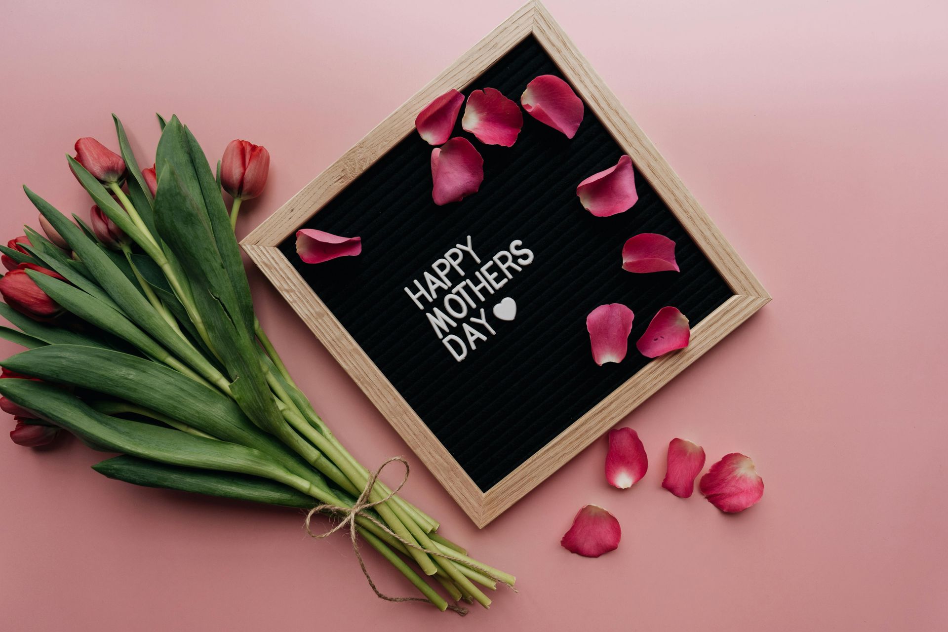 Muttertagsstrauss mit rosa Tulpen und Rosenblättern neben einer Karte mit der Aufschrift „Alles Gute zum Muttertag“.