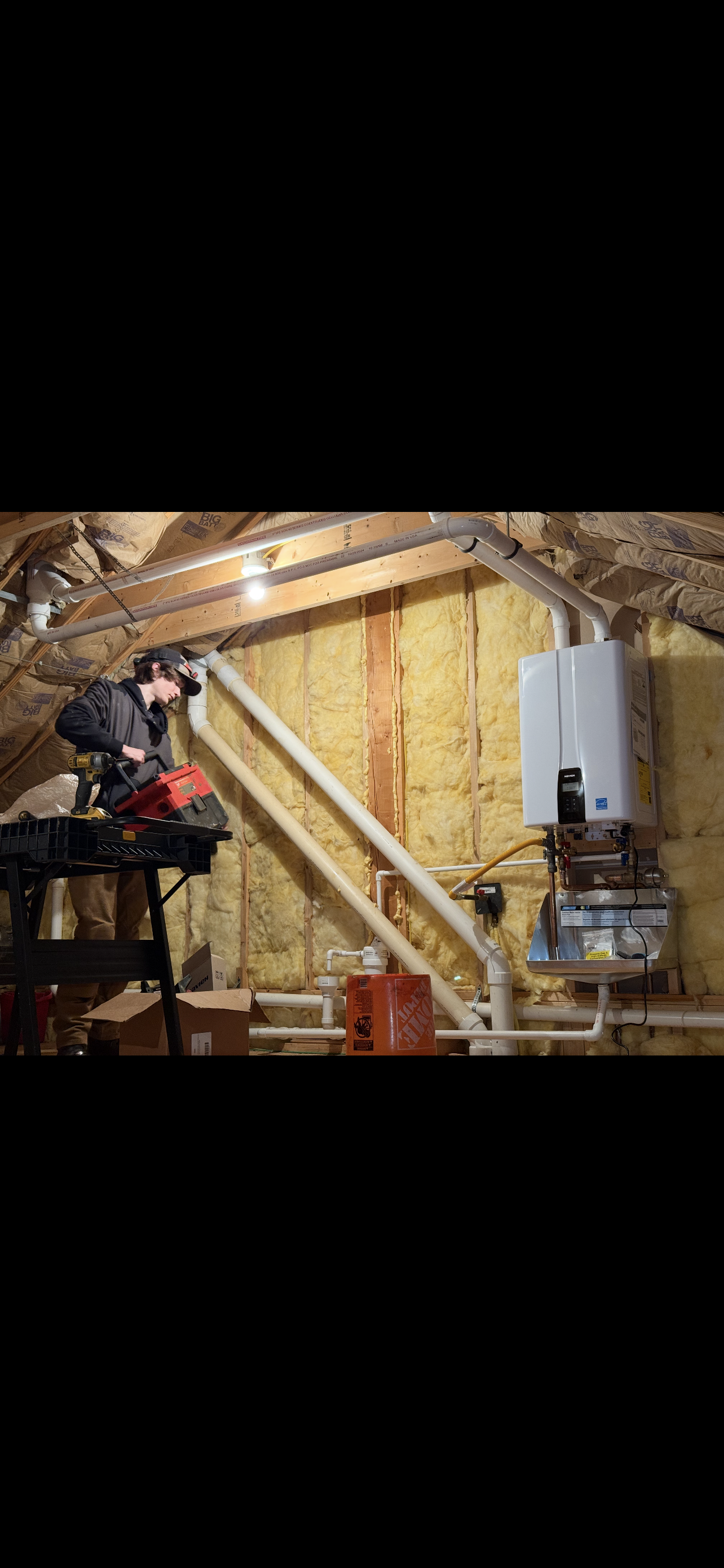 A newly installed water heater with supporting pipes and a ladder in an attic.