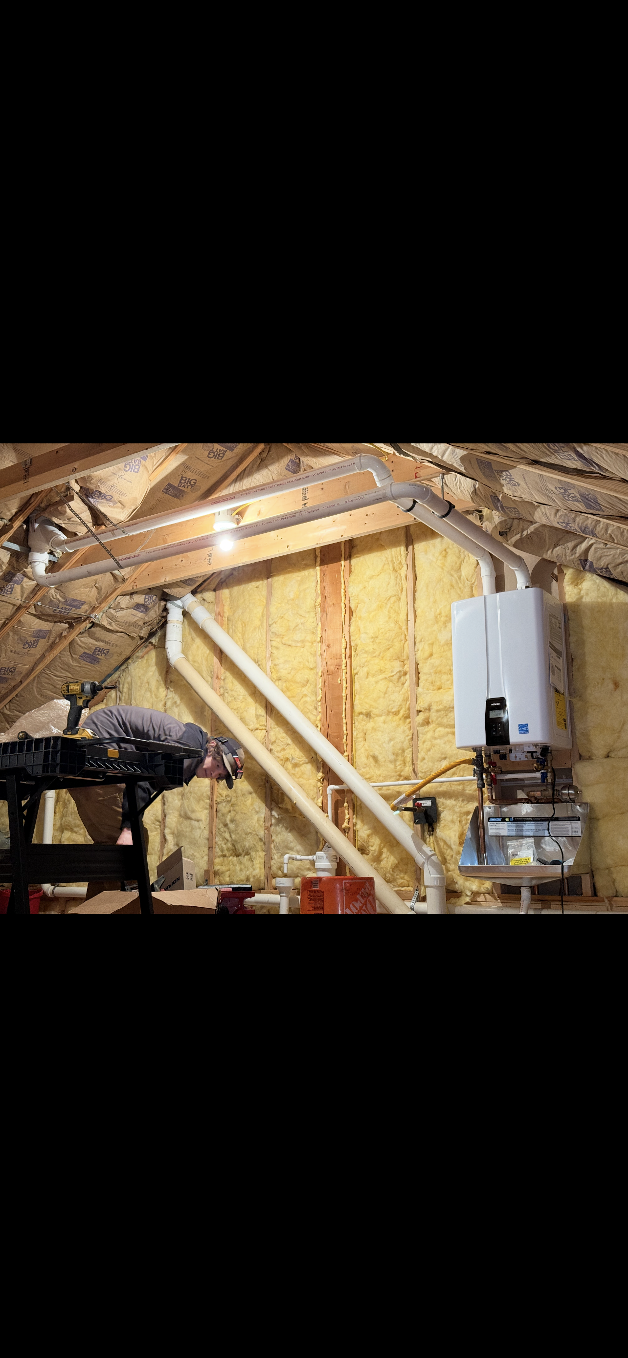 Attic with a water heater, pipes, and wooden framing.