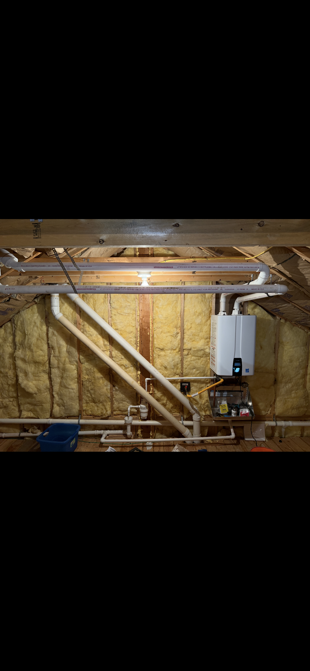 Water heater installed in an attic, supported by wooden bracing. Yellow insulation lines the wall.