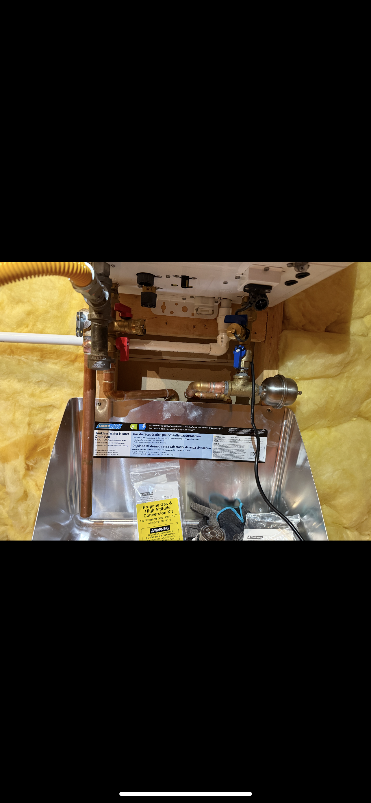 Plumbing and electrical components, including copper pipes, on a white and yellow insulated board in a wall.