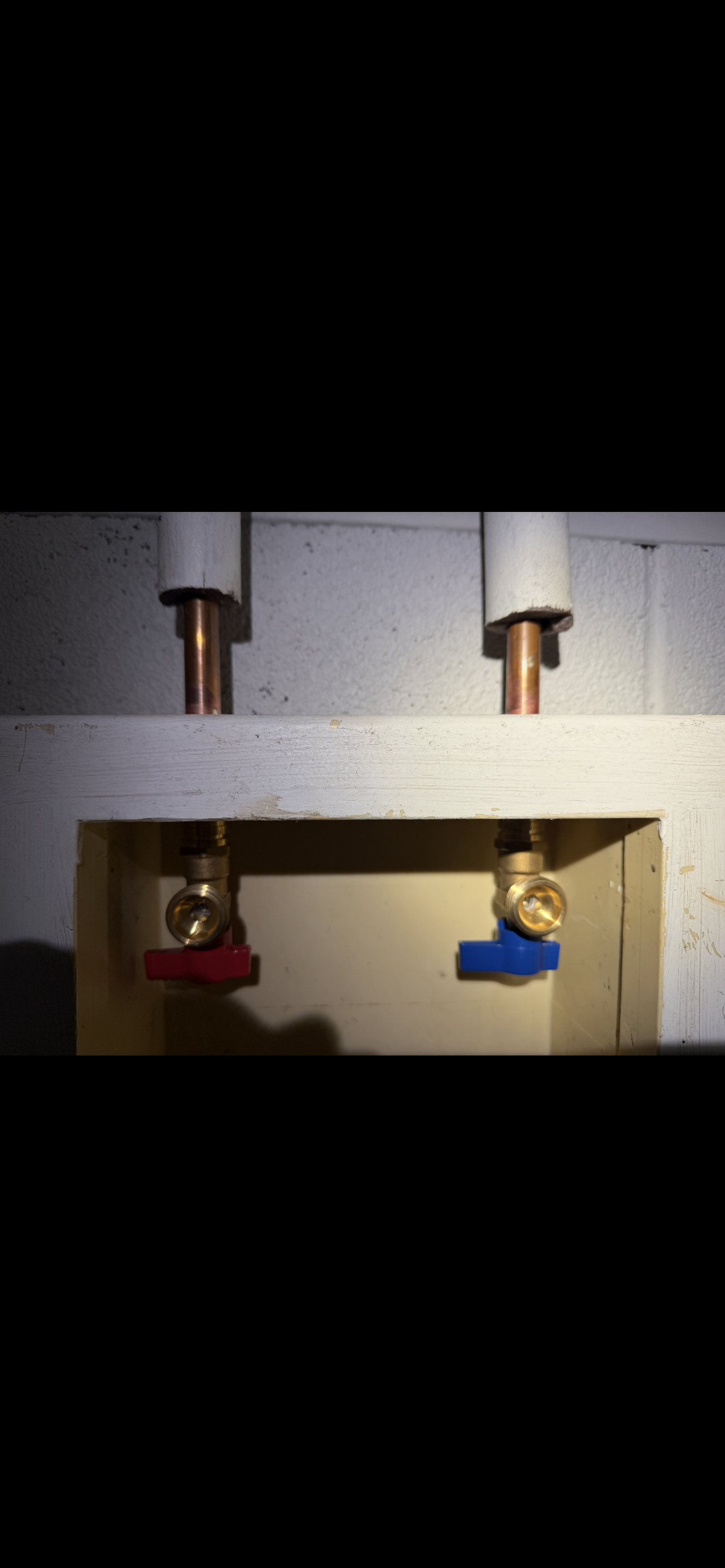 Pipes with red and blue valves, likely hot and cold water supply, inside a wall cutout.