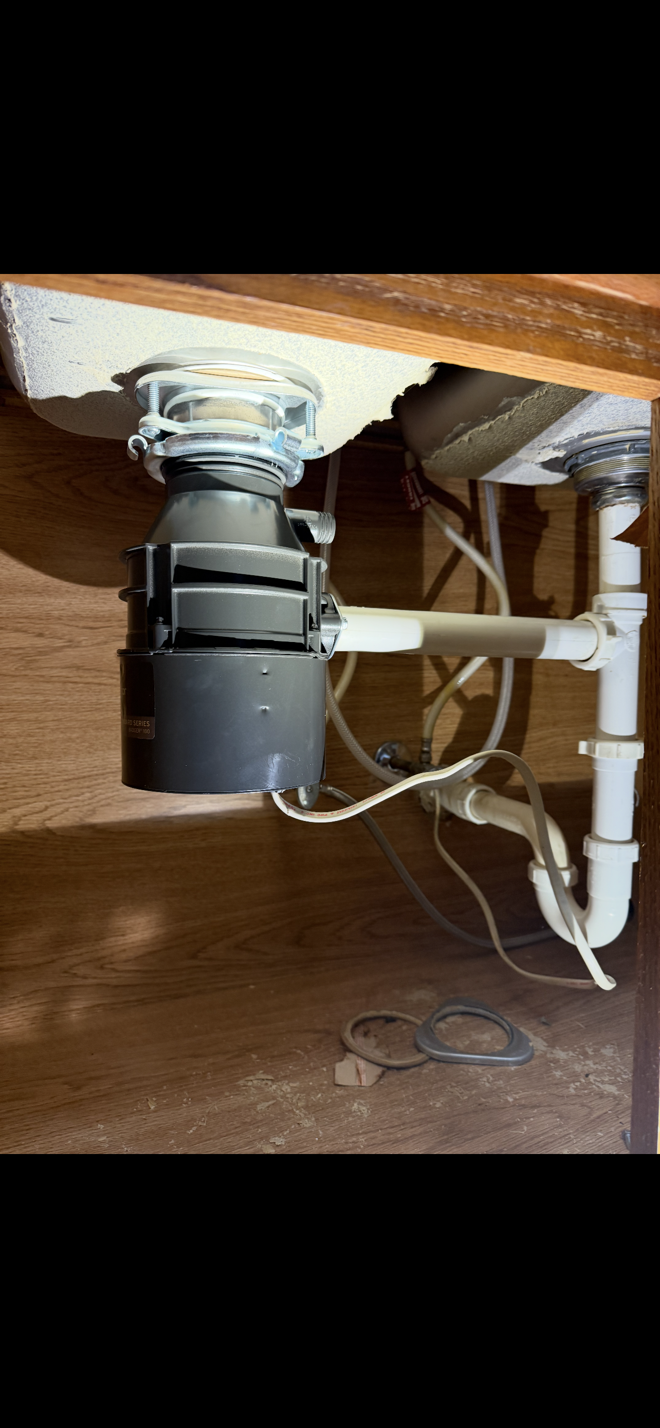 Under-sink view of a garbage disposal unit connected to pipes and wires.