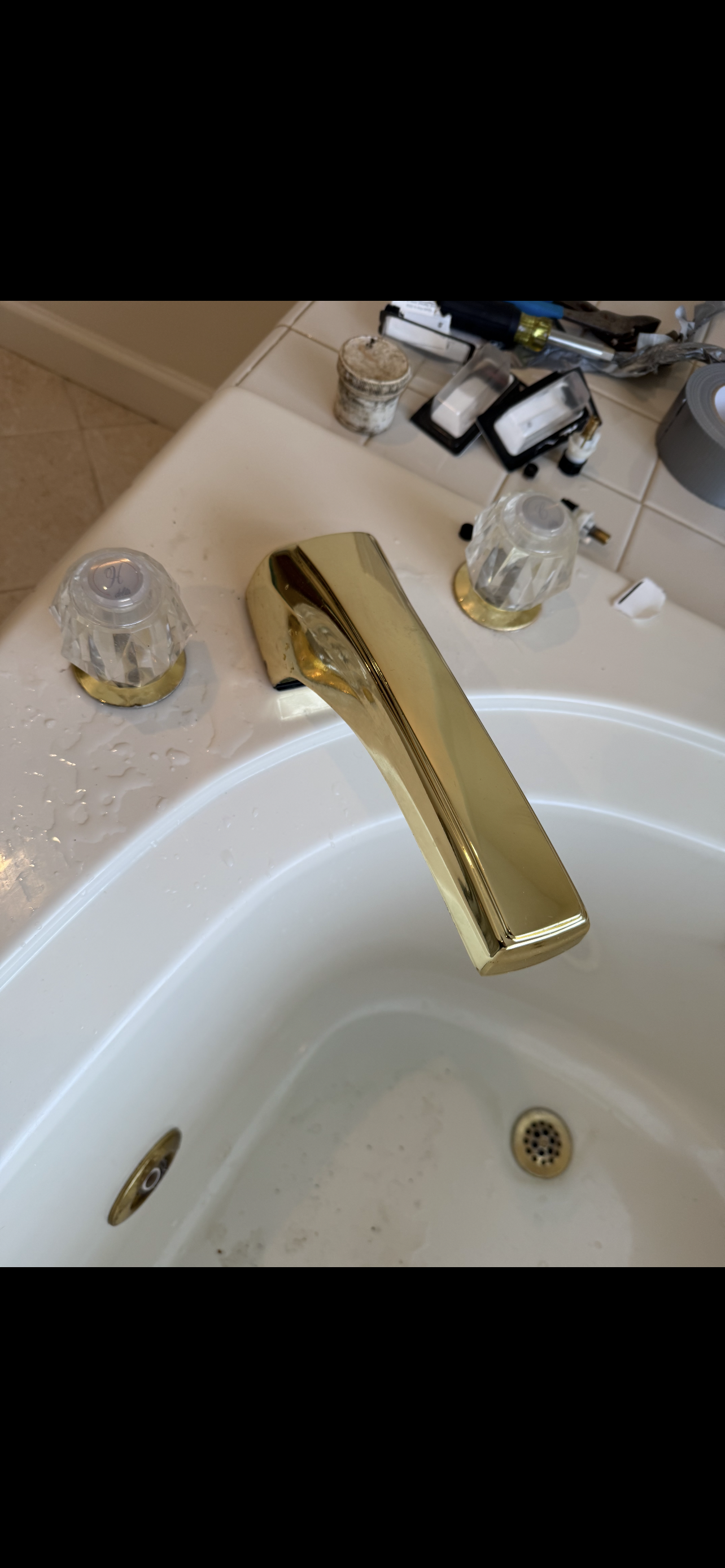 A gold faucet on a white bathtub, with handles on the side.