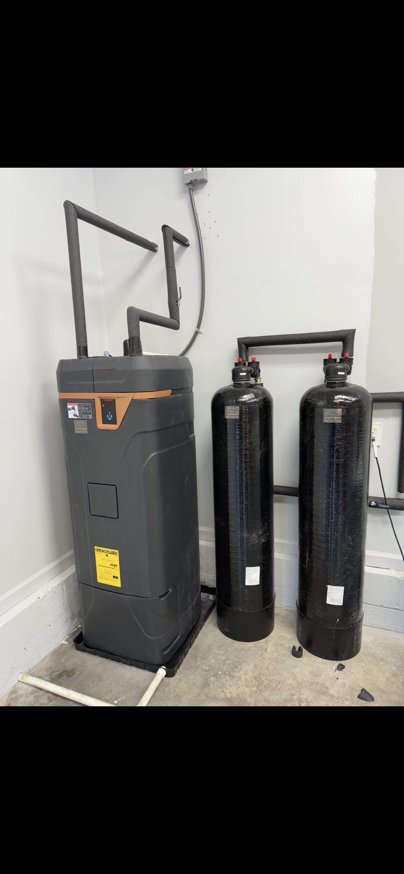 A water heater with two black tanks in a utility room.