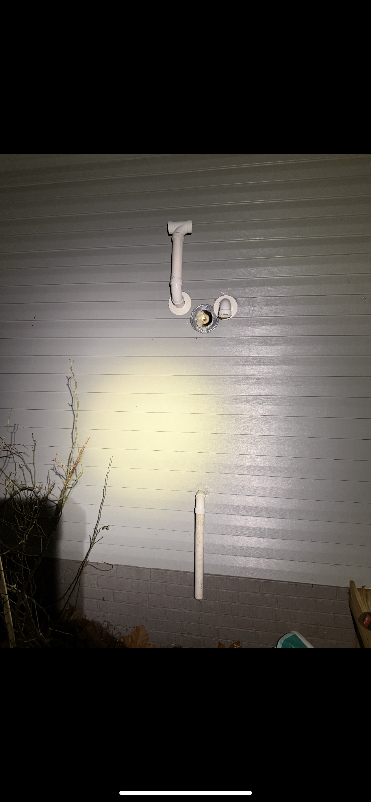 Overhead view of a white pipe system on a wet surface, illuminated by a yellow light.