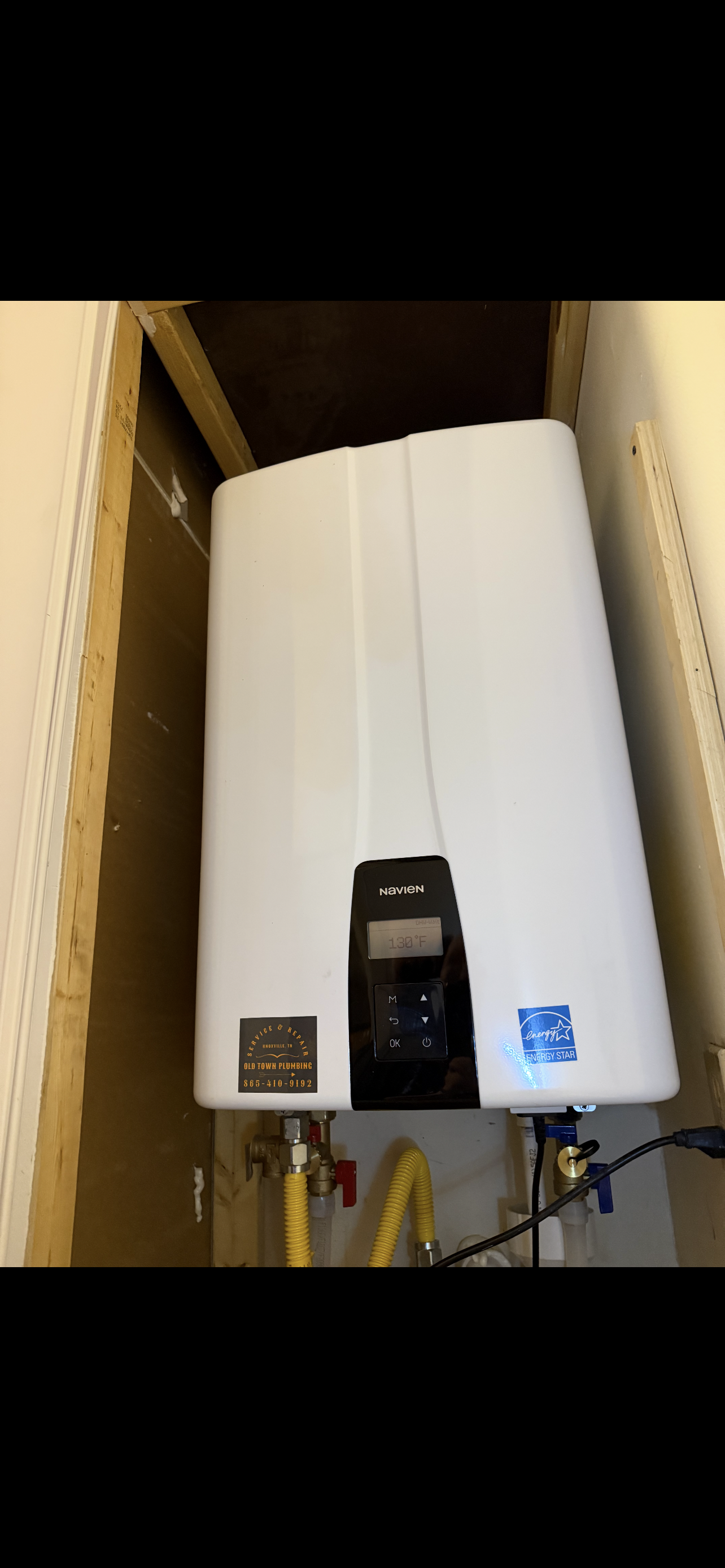 A white tankless water heater installed in a cabinet. Yellow gas line visible.