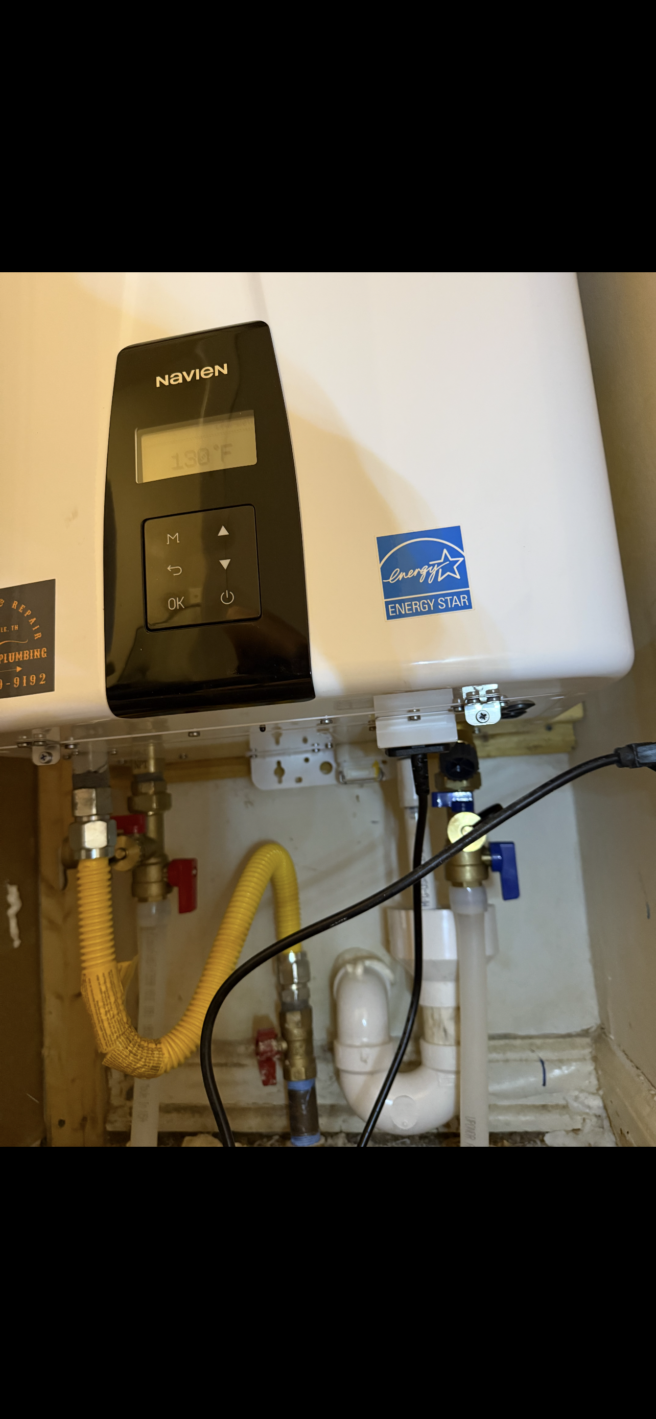 A gas water heater unit with attached pipes, valves, and a control panel.