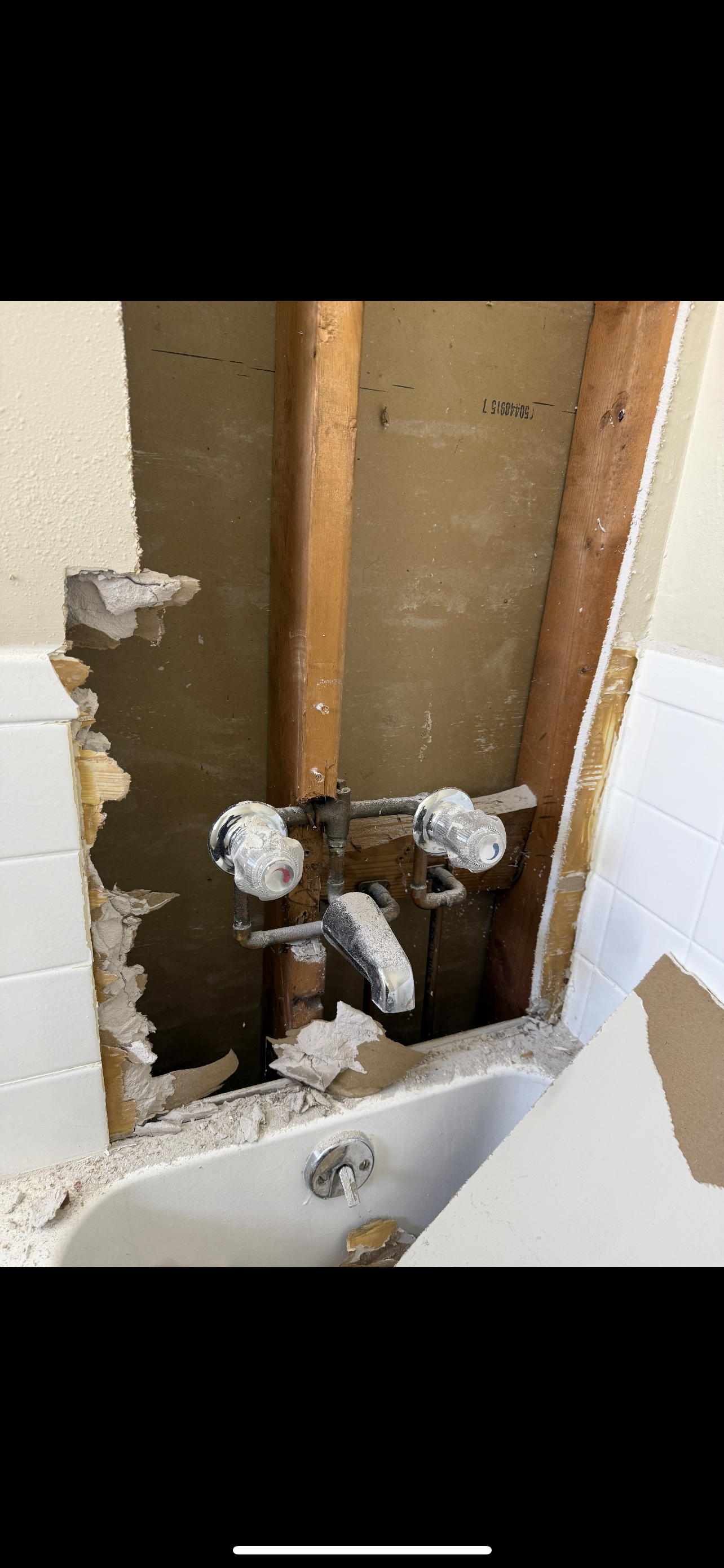 Bathroom plumbing rough-in with damaged wallboard, a bathtub is visible.