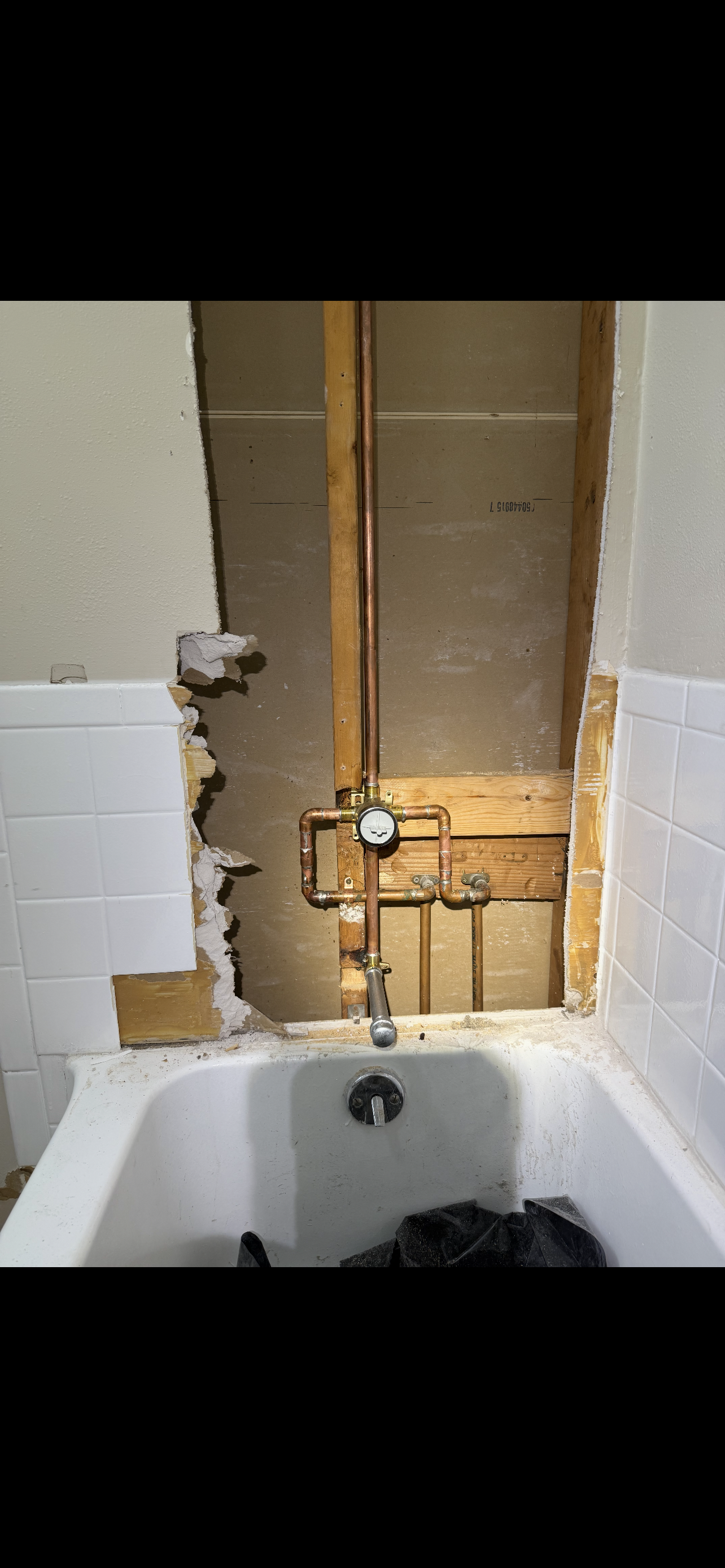 Bathroom with exposed plumbing and tub, wall damaged.