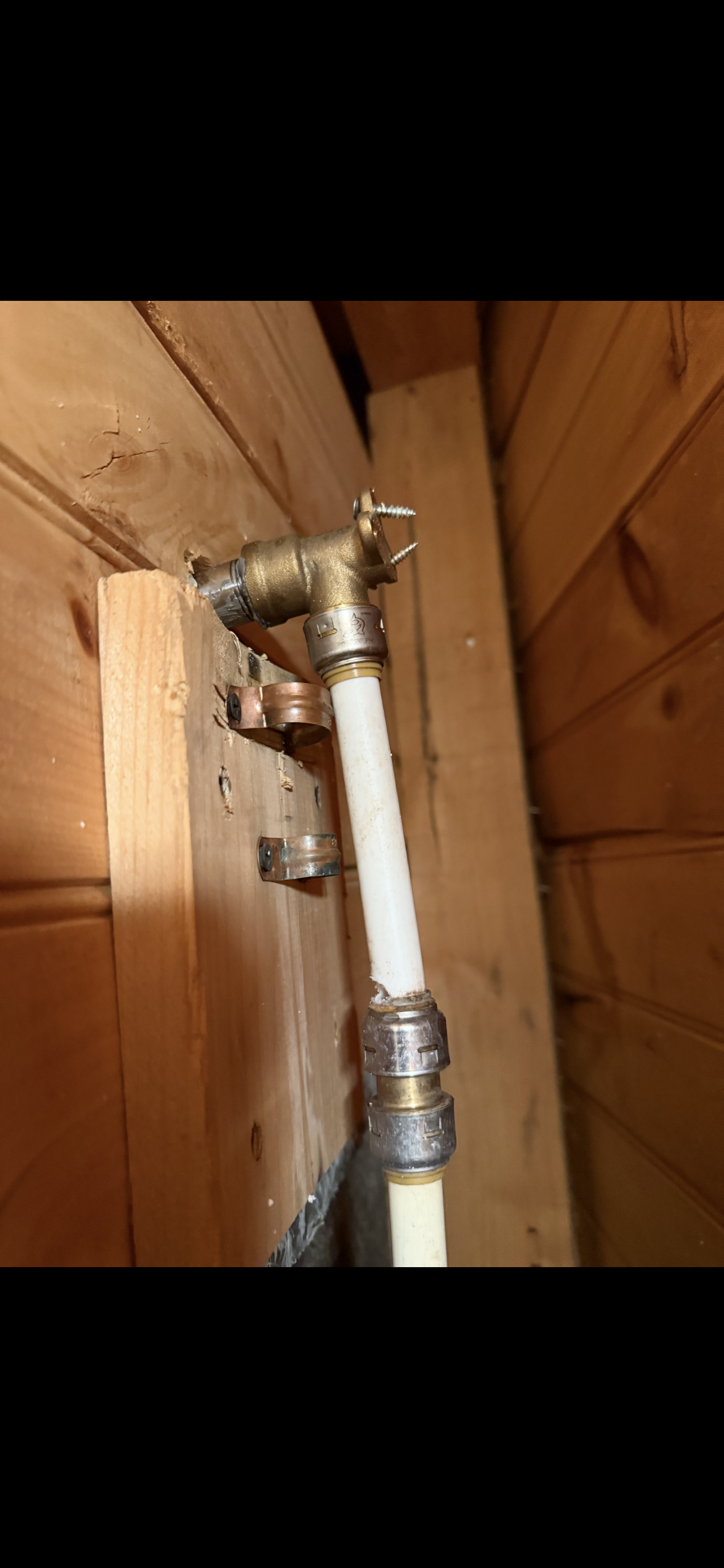 Pipes and plumbing, brass pipe with white tubing, installed against wooden boards.