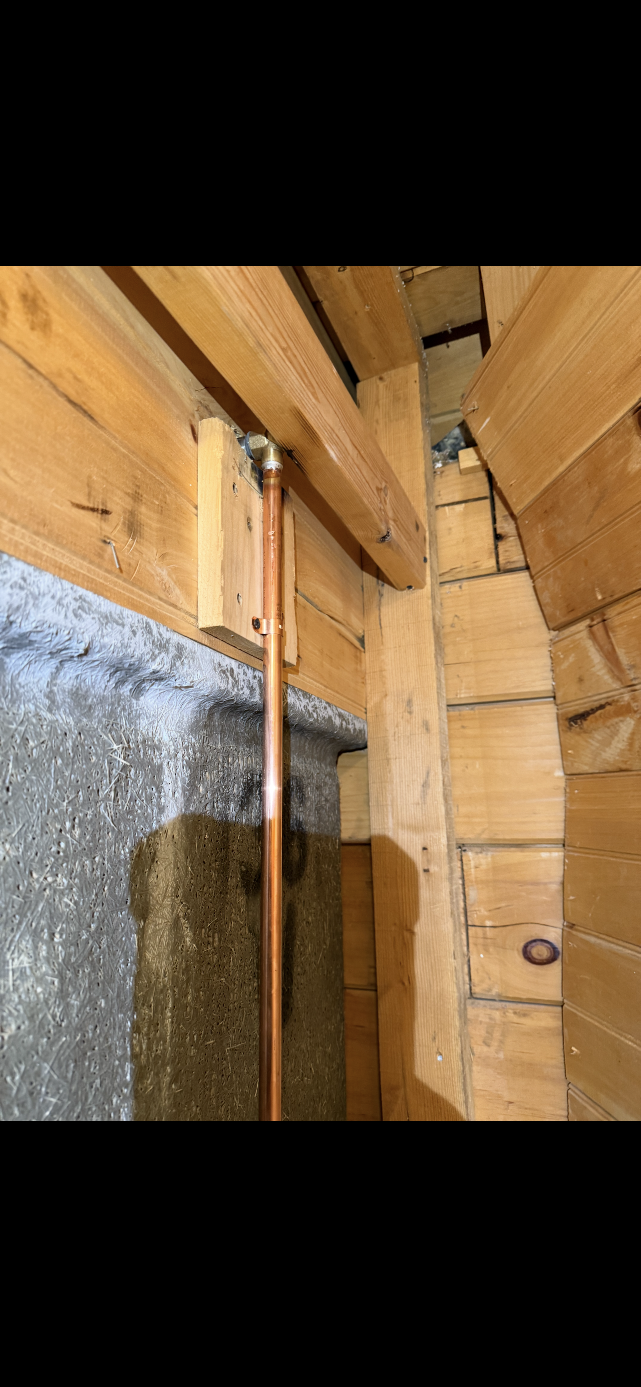 Copper pipe runs vertically along a wood frame; concrete wall on left.