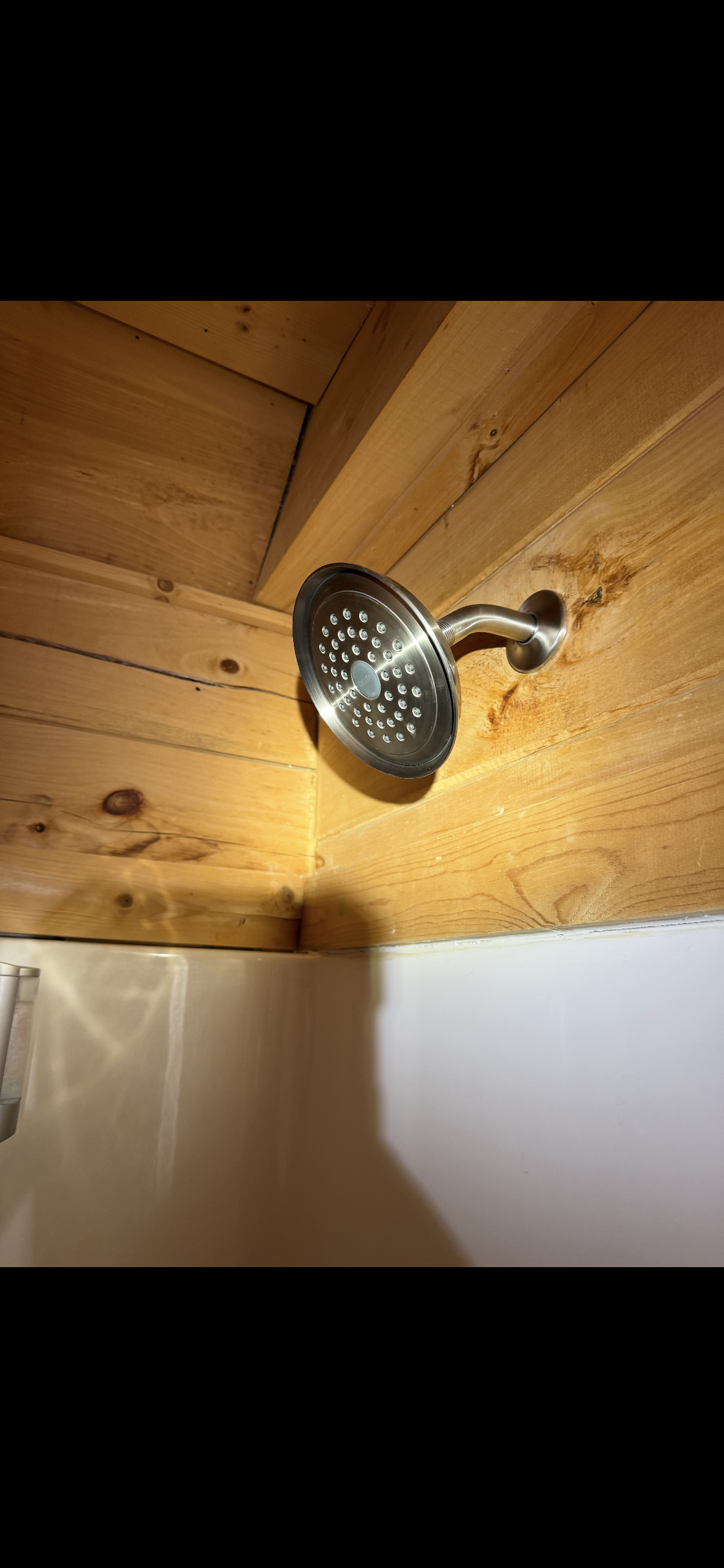 A stainless steel showerhead attached to a wooden ceiling in a bathroom.