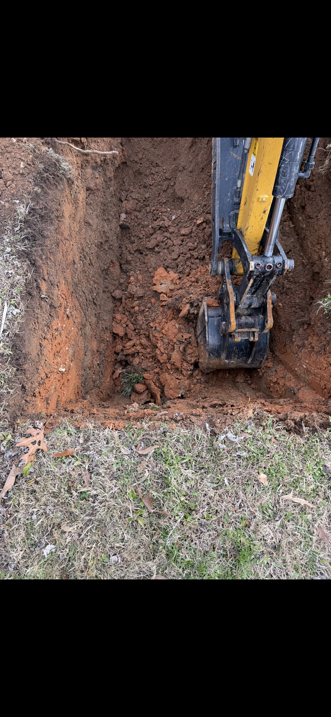 An excavator digging a trench in brown soil. Grass in the foreground and a black frame.