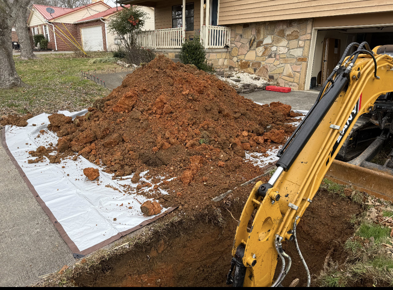 Yellow excavator digging near a house, with a pile of dirt on a tarp next to a sidewalk.