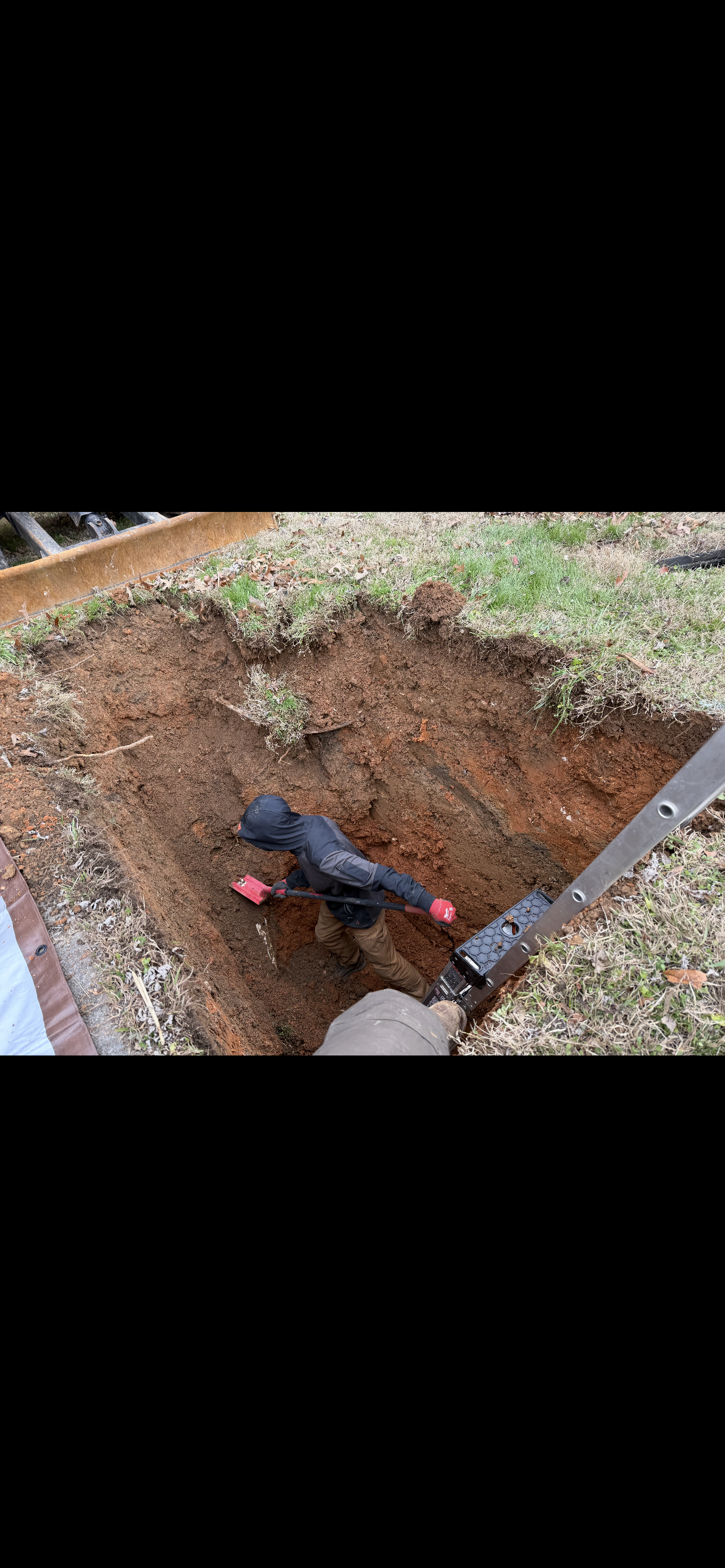 A black garden hose with red ends lies in a patch of dirt, surrounded by grass.