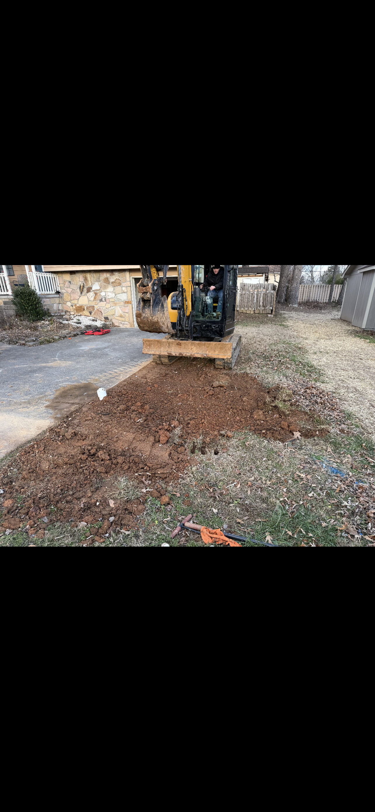 A yellow excavator digging in a yard, with a pile of dirt in front.