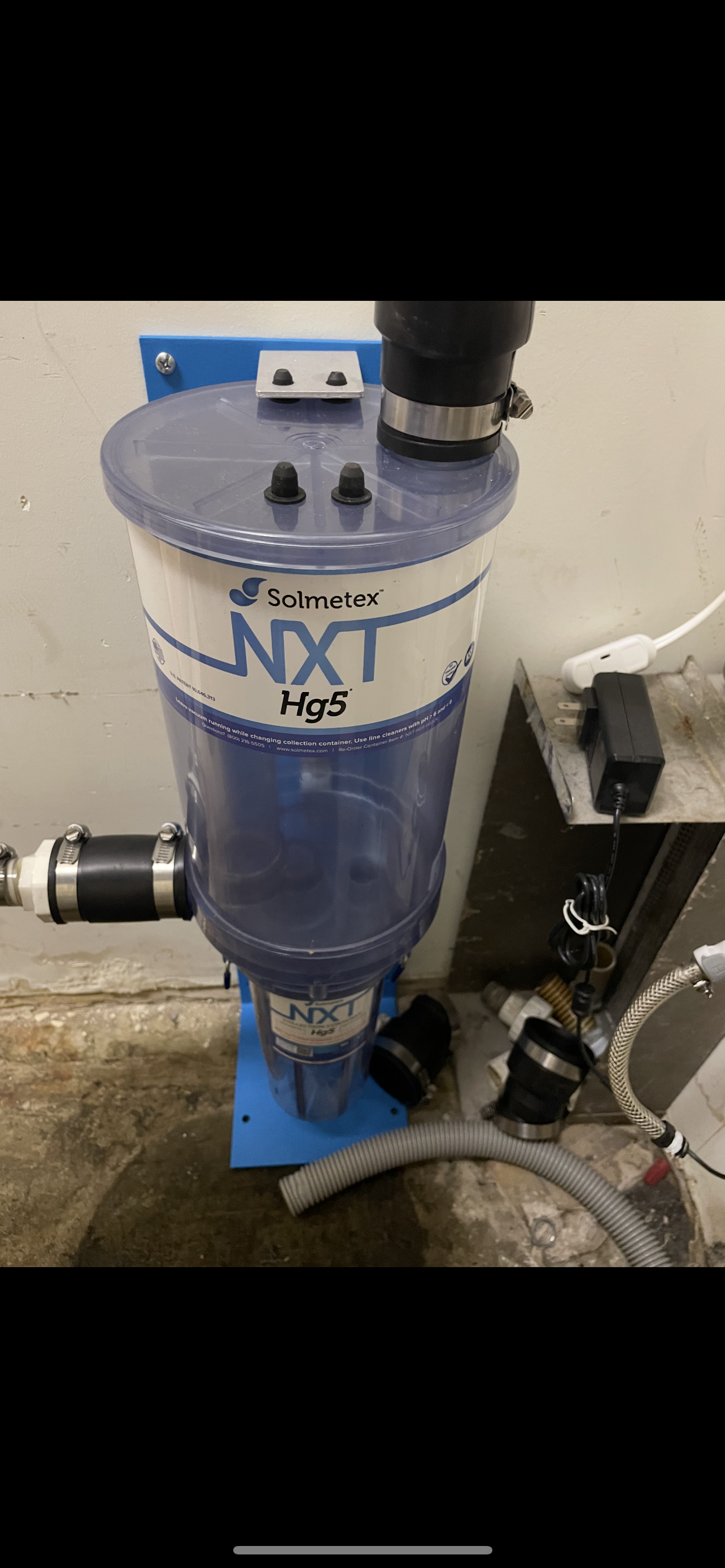 A blue and white water filter with the word “NXT” is mounted on a wall in a concrete setting.