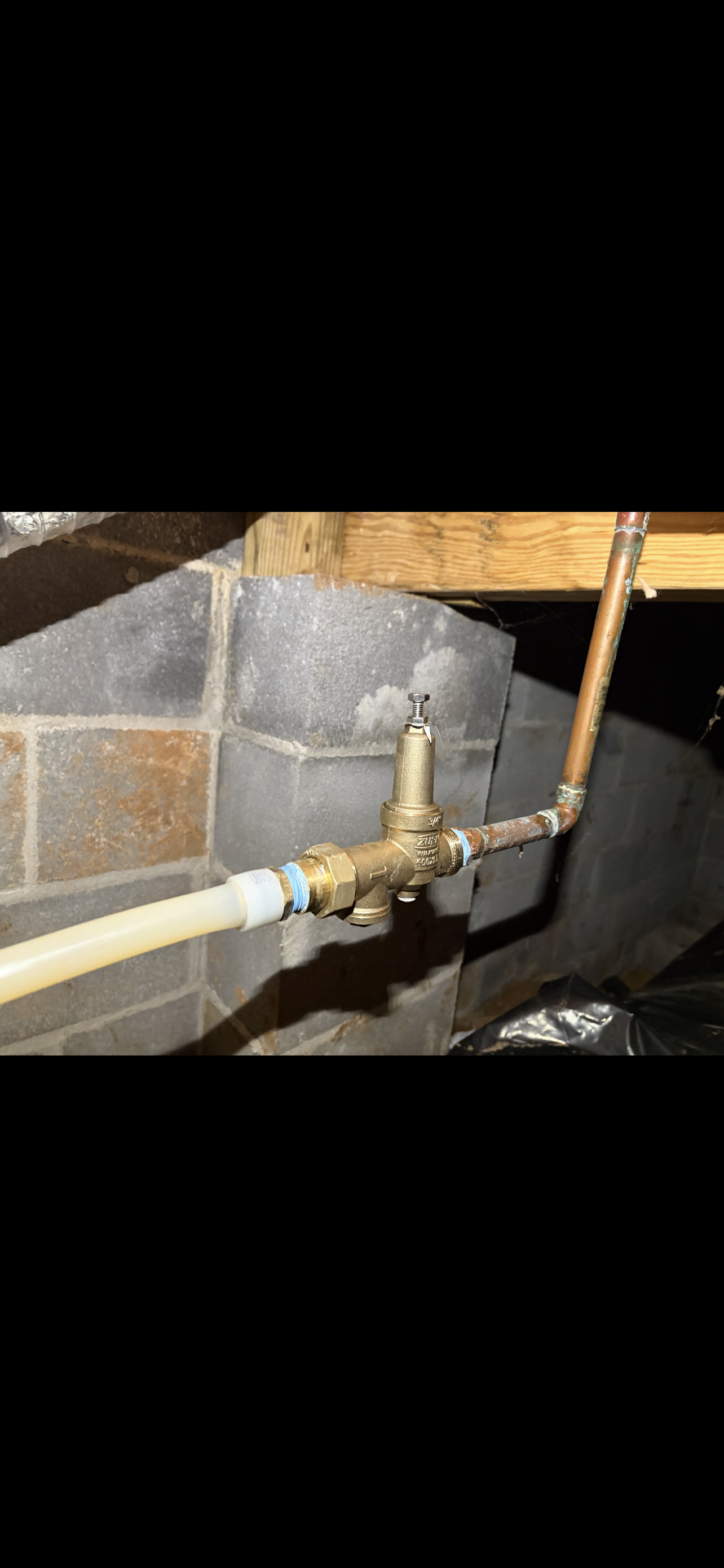 Plumbing system with copper and PEX pipes attached to a brass valve against a cinder block wall.