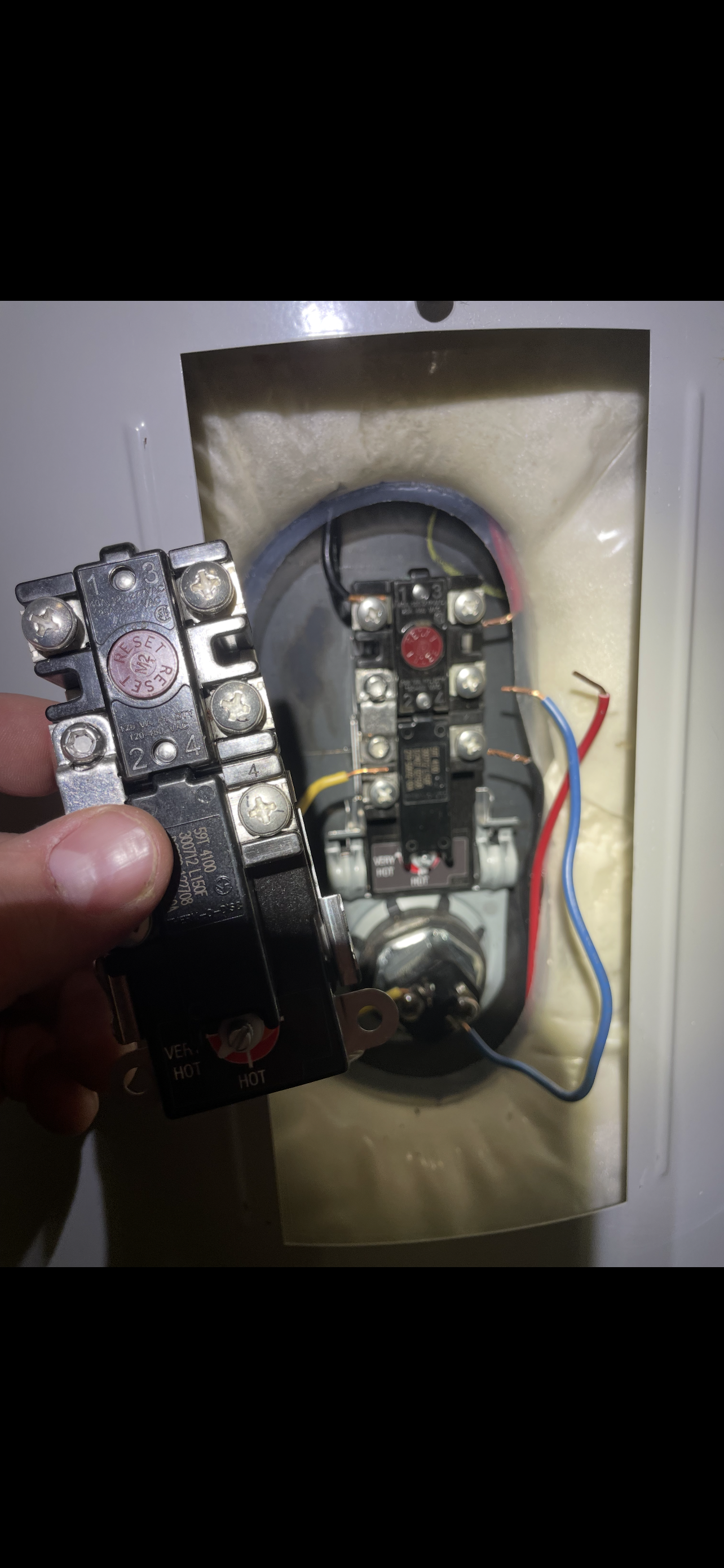 Close-up of a damaged water heater element and thermostat. The element is held in a hand.