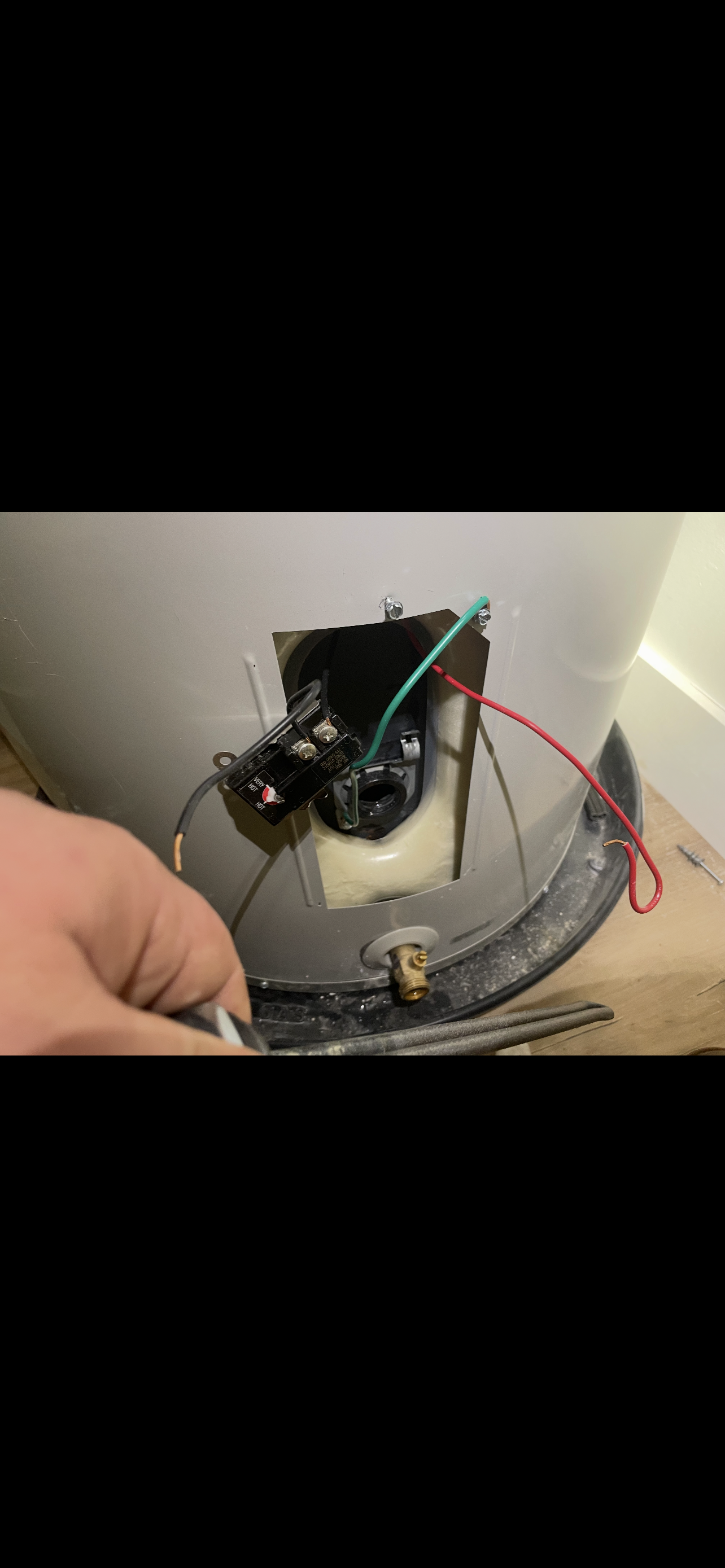 A person's hand holding a wire near a water heater's electrical components.