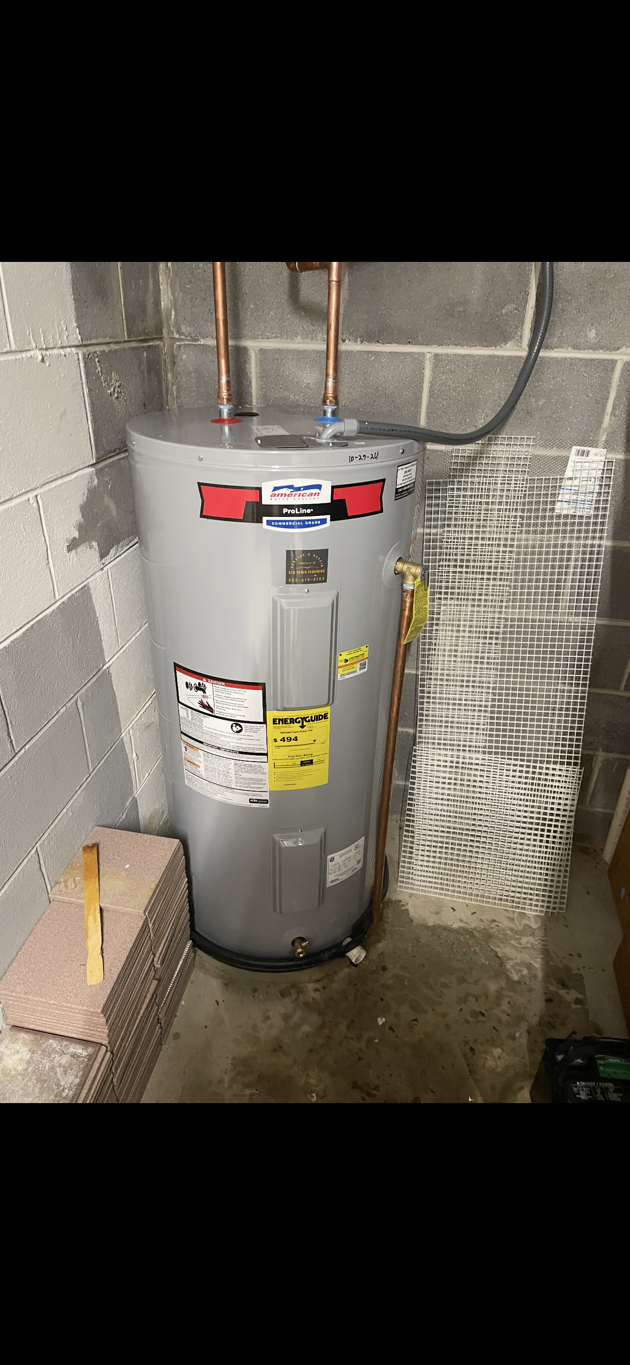 Water heater in a basement setting, with copper pipes and brick wall.
