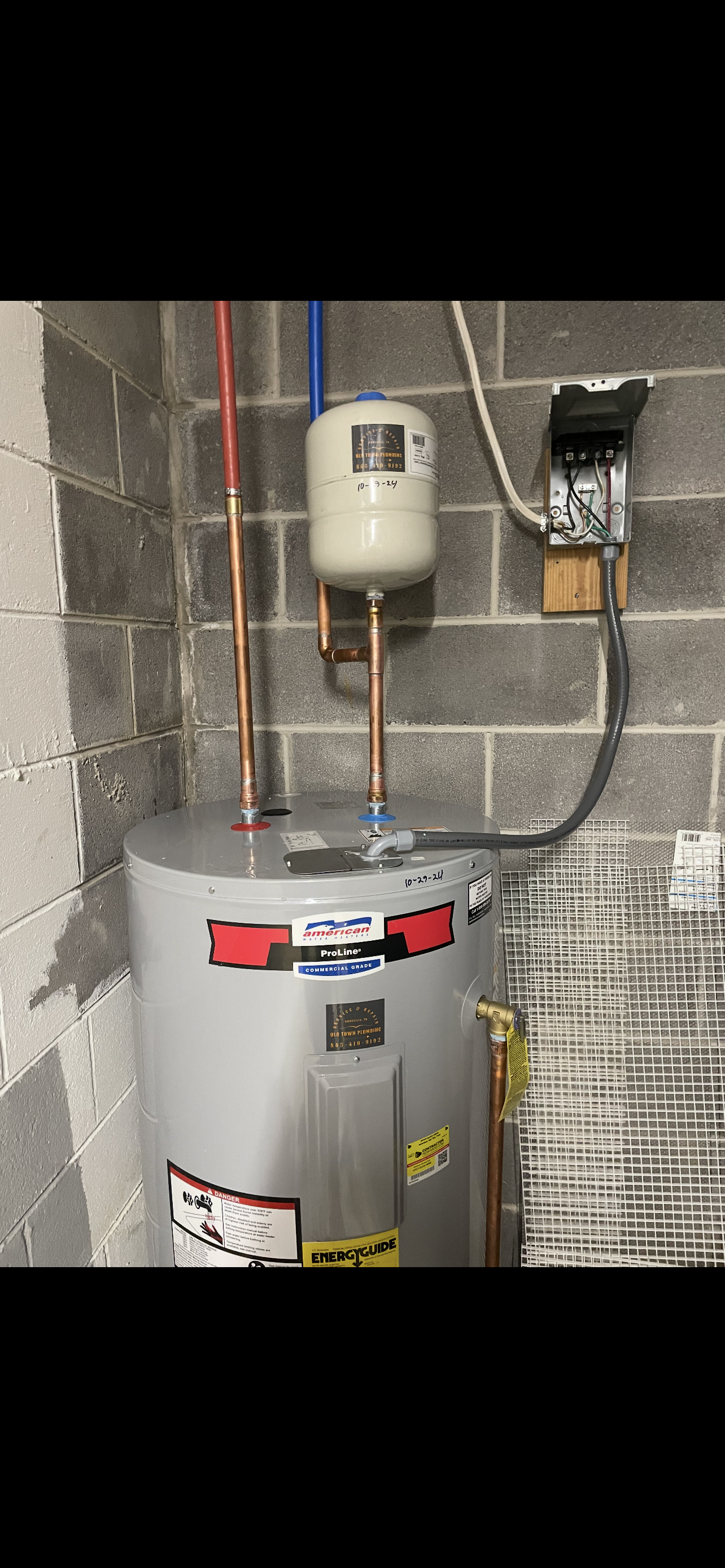 Water heater in a basement, with expansion tank and electrical panel.