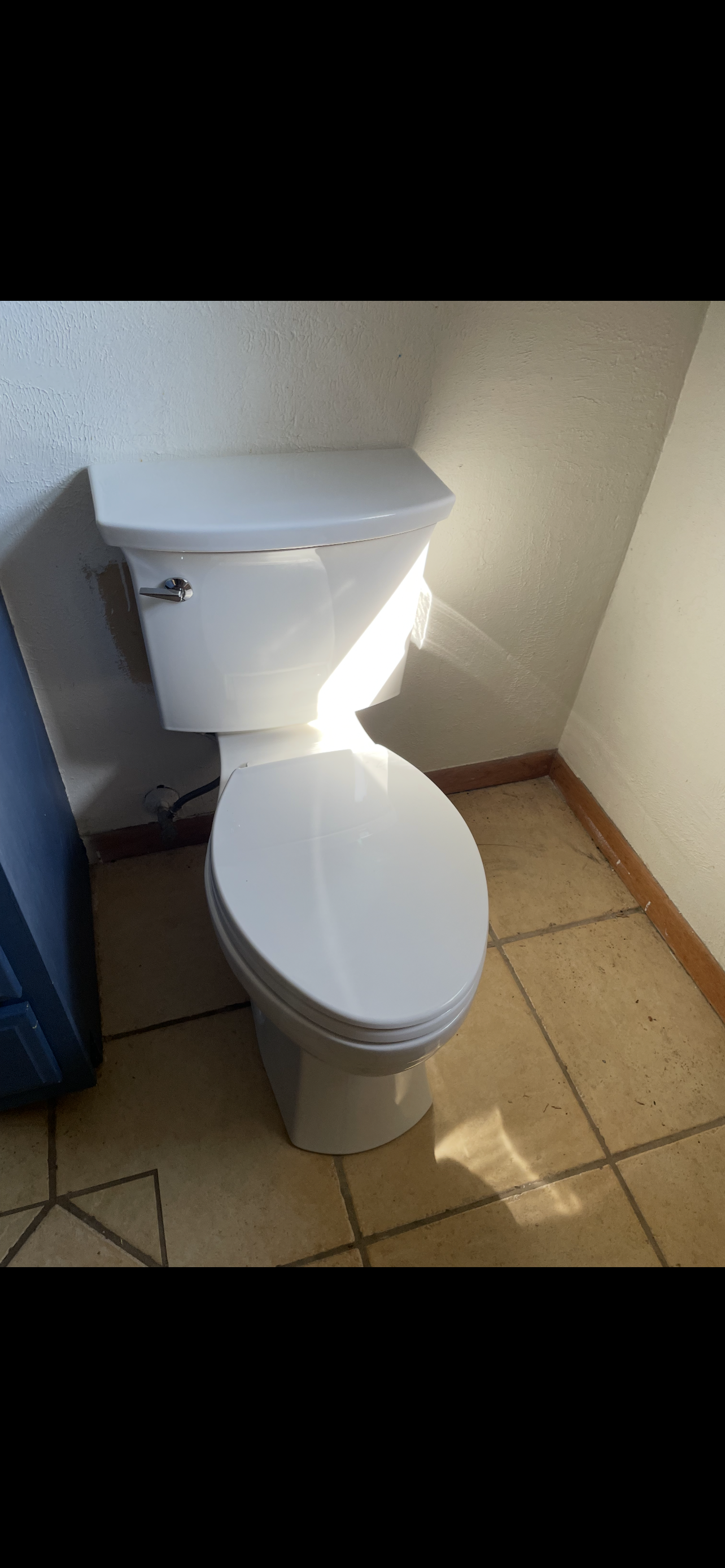 White toilet in a small bathroom. Bright sunlight shines on the toilet.