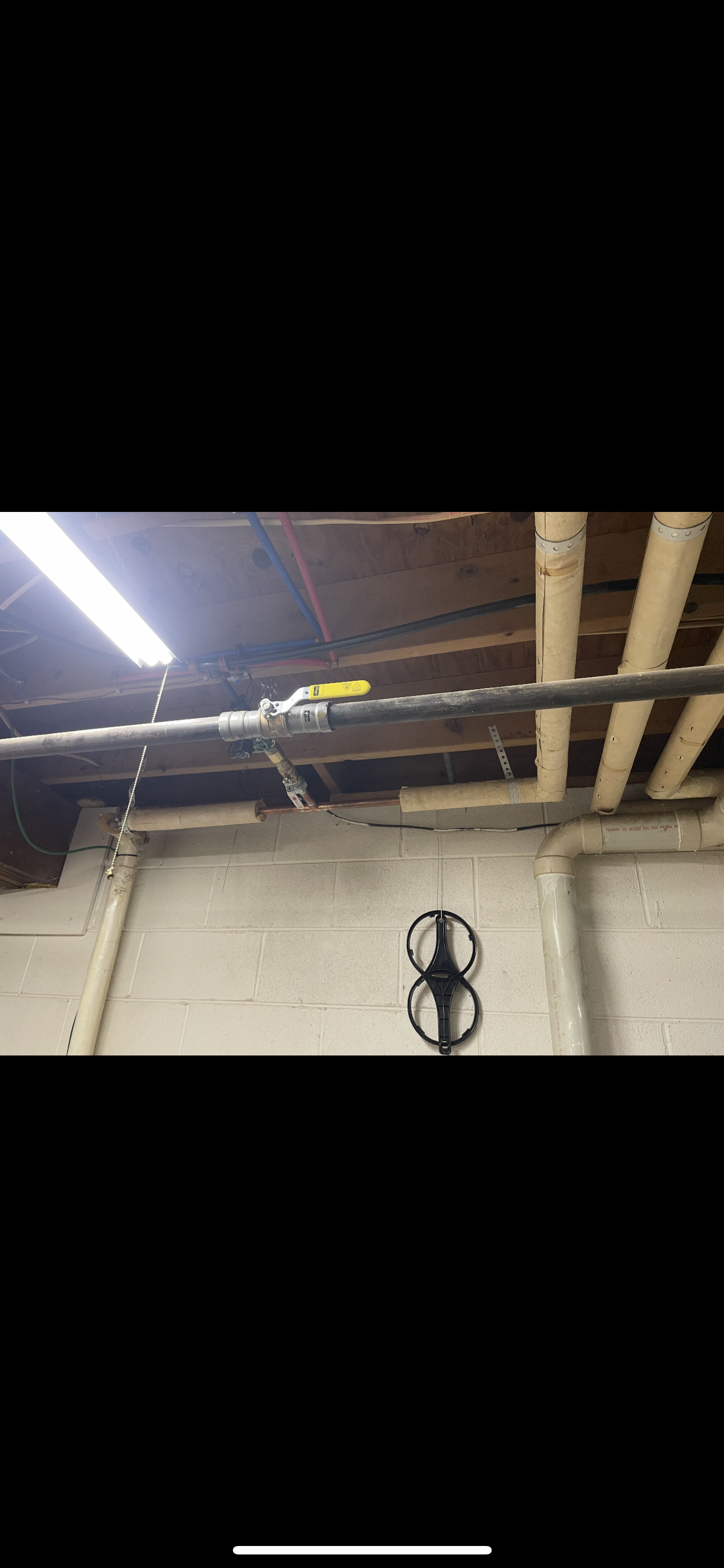 Ceiling pipes with valve and a hanging device in a dimly lit room.
