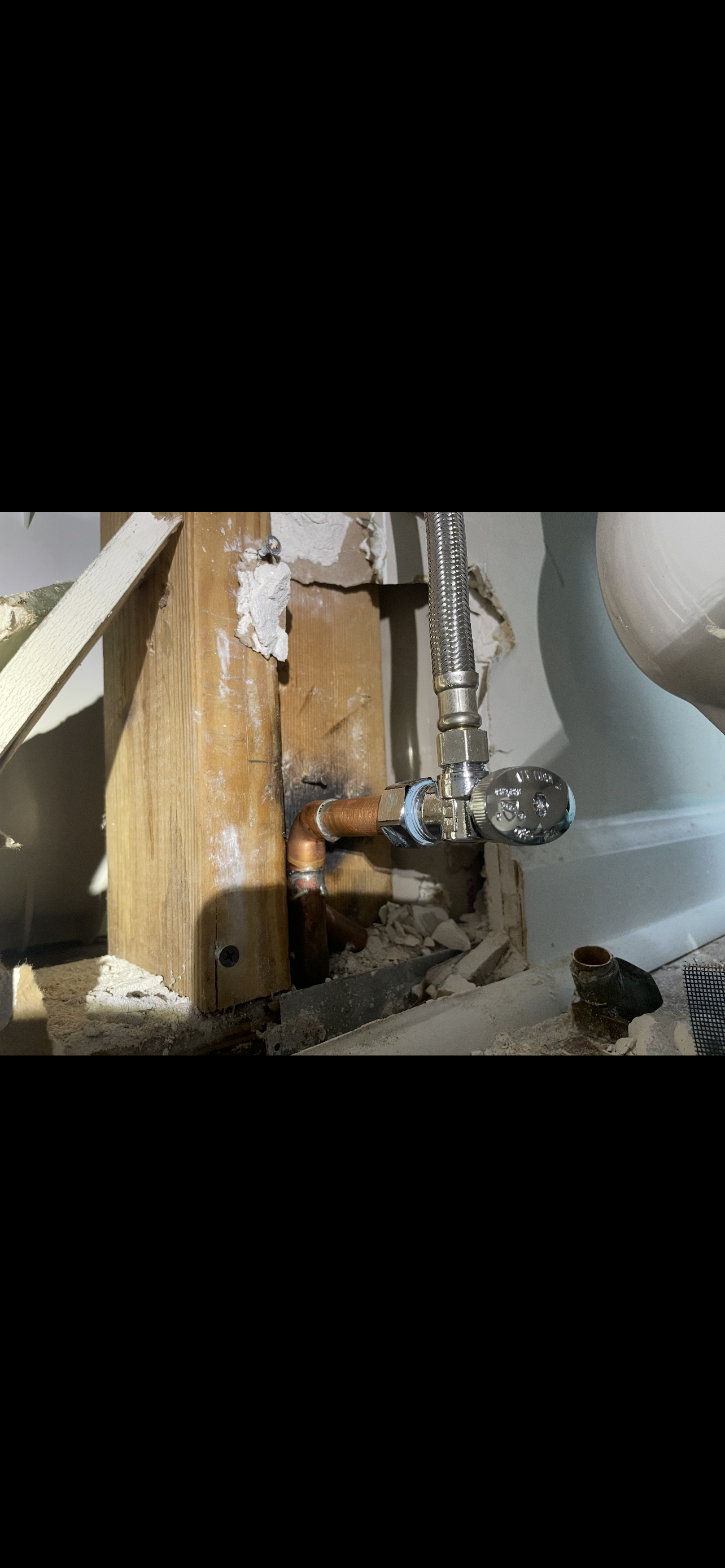 Copper pipe plumbing near wooden support. A shut-off valve is visible.