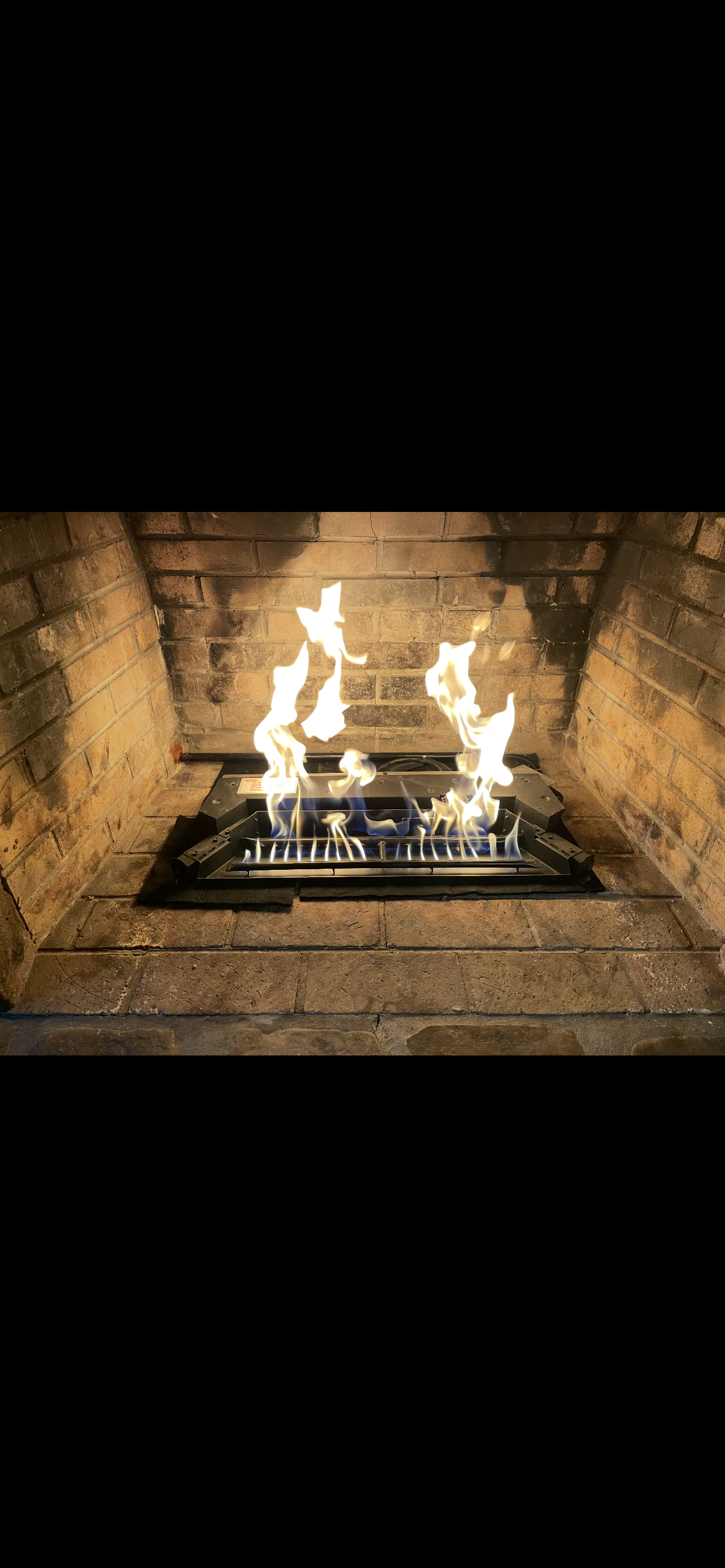 A lit fireplace in a brick hearth, flames rising from gas logs.