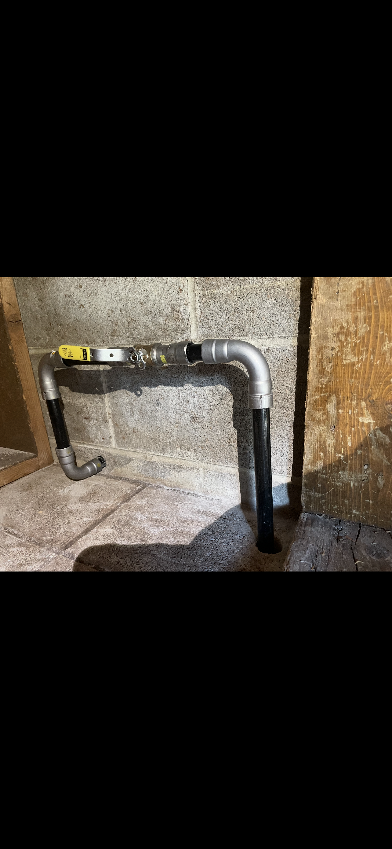 Metal pipes with a valve are attached to a concrete wall, in a dark indoor setting.