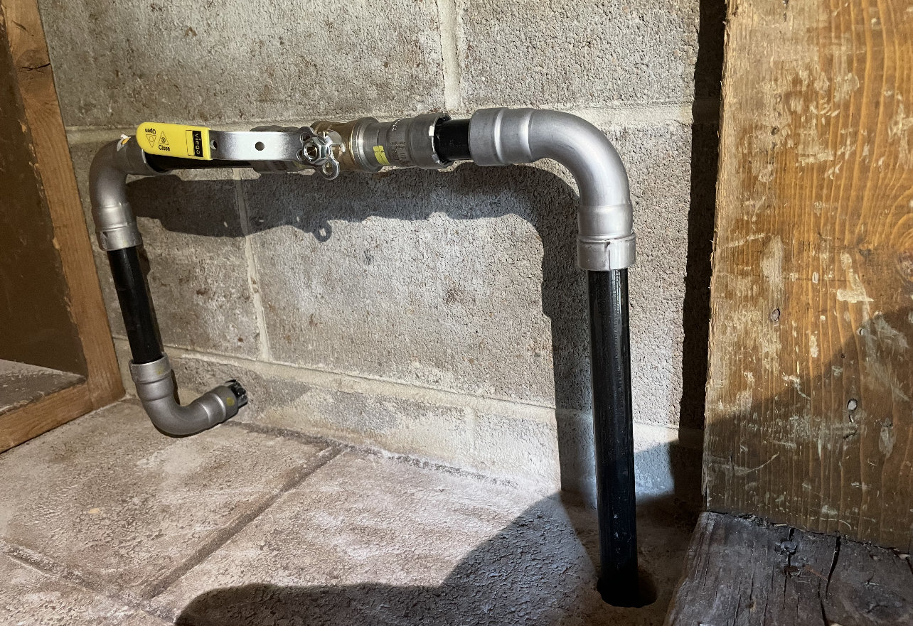 Gas pipe assembly with a yellow valve, set against a concrete wall.
