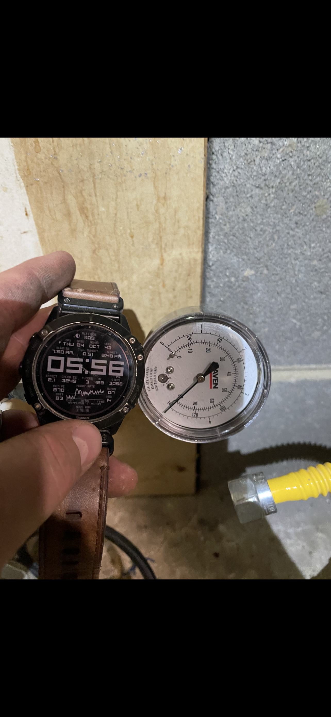 Hand holding a digital watch and a gauge. Watch shows 05:56. Gauge needle at about 4.